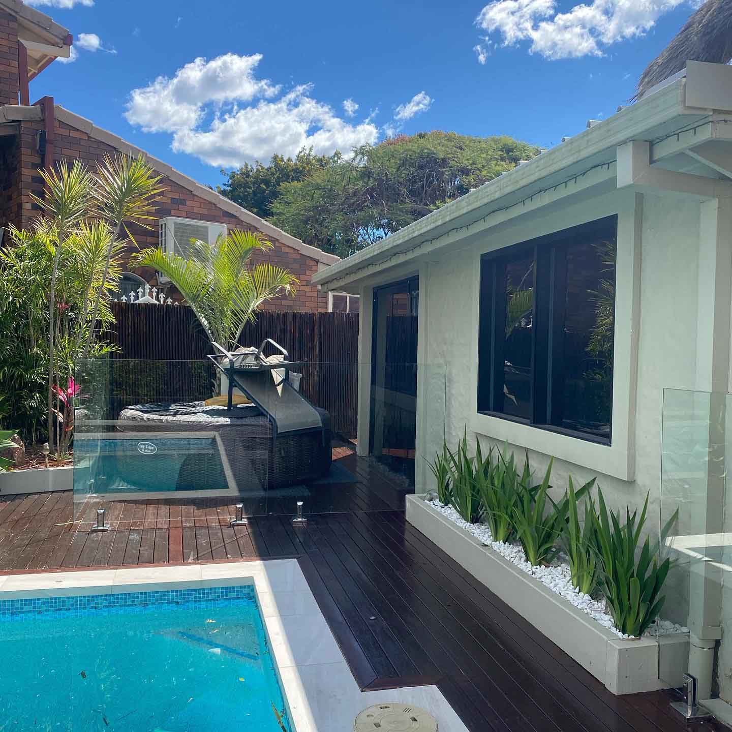 Dark oiled timber deck around a pool and spa with white planter boxes