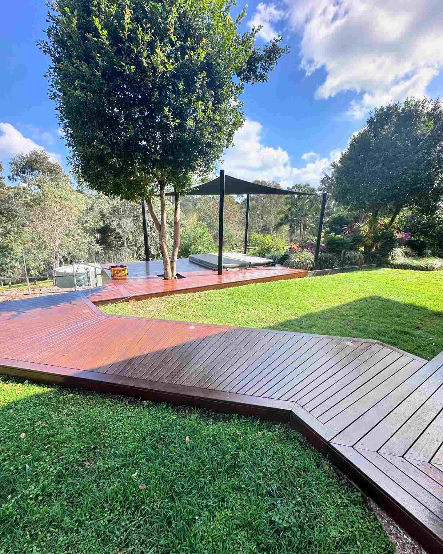Portrait view of the angled timber deck path across a lawn towards a shade sail