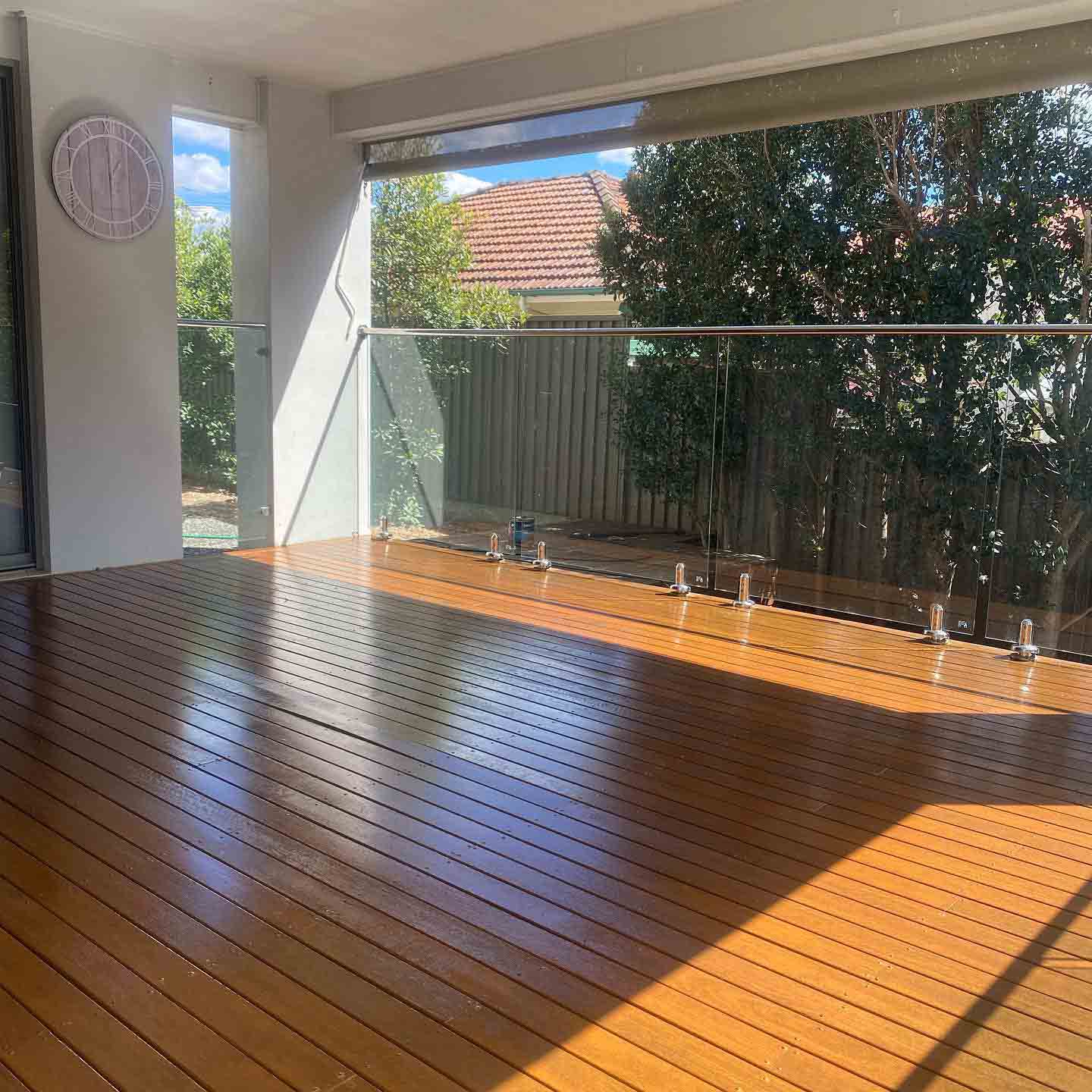 Glossy oiled timber deck with glass balustrade under a patio