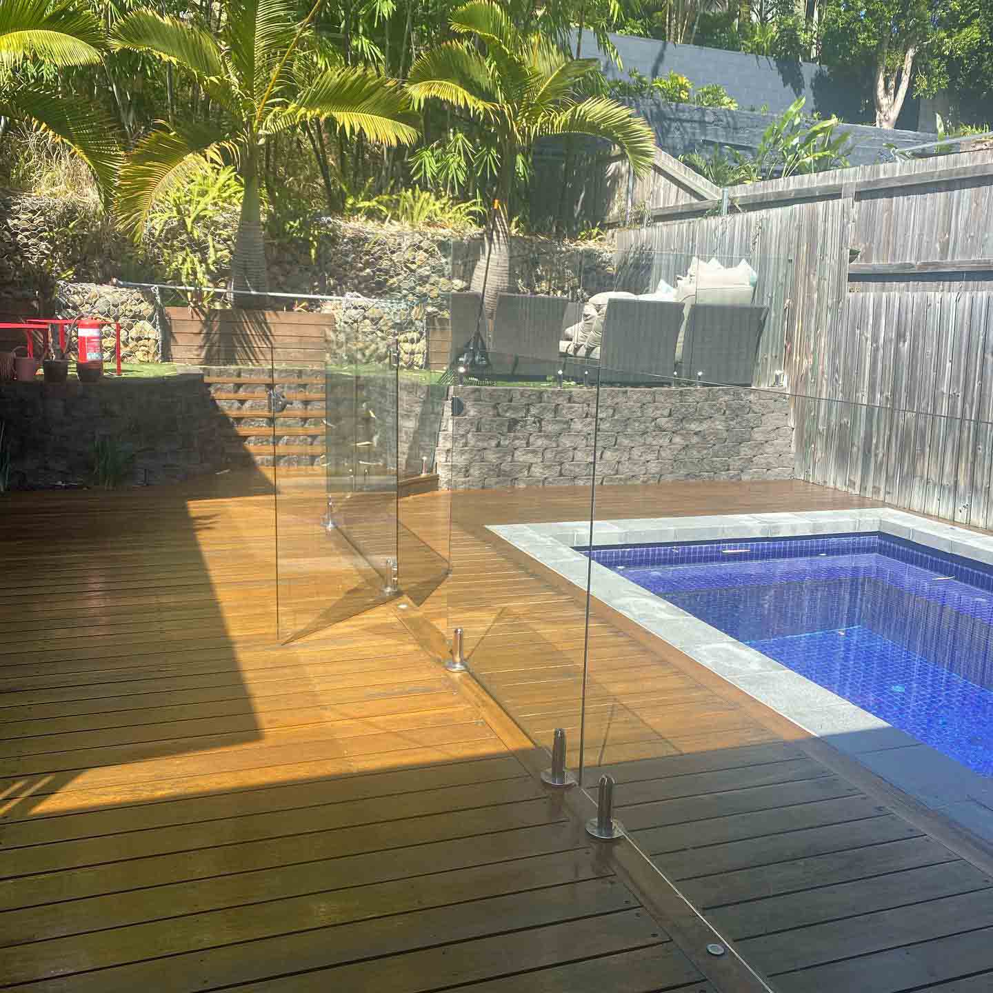 Oiled timber deck with glass pool fencing and a gabion wall