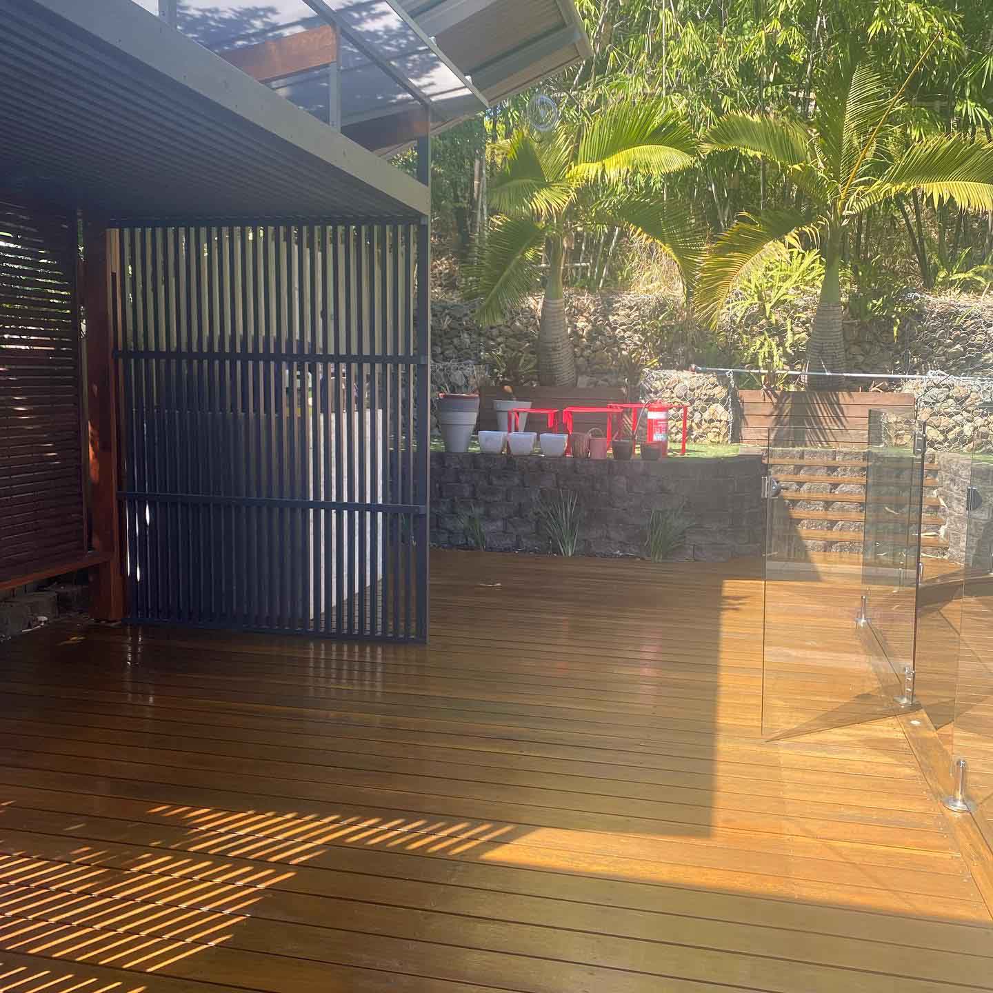 Oiled timber deck with a dark slatted screen and glass pool fence