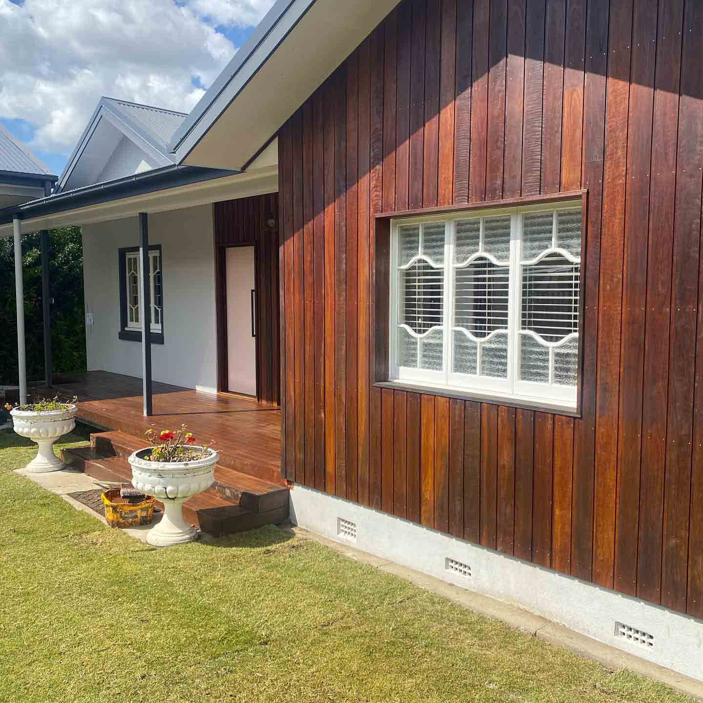 Oiled timber verandah and steps beside dark vertical timber cladding on a lawn