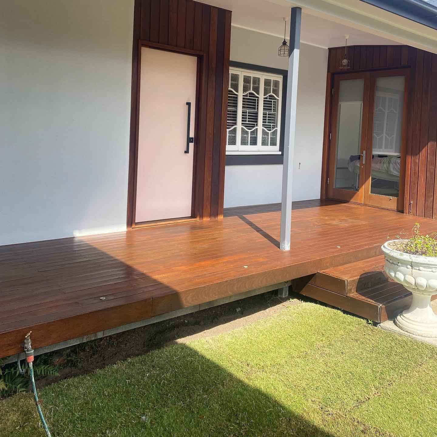 Oiled timber verandah with steps down to the lawn and white urn planters