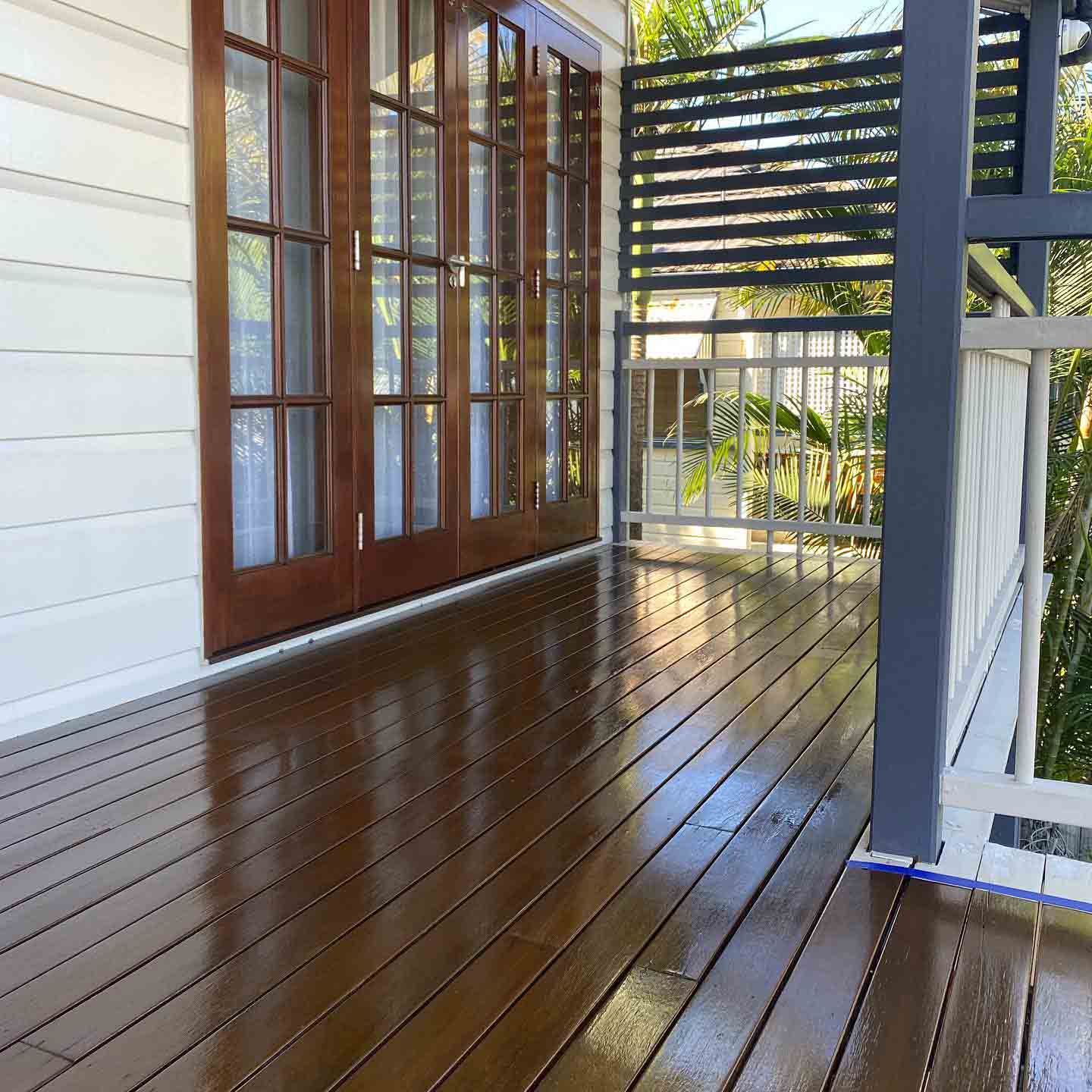 Glossy wet oiled timber deck along timber French doors and a slatted screen