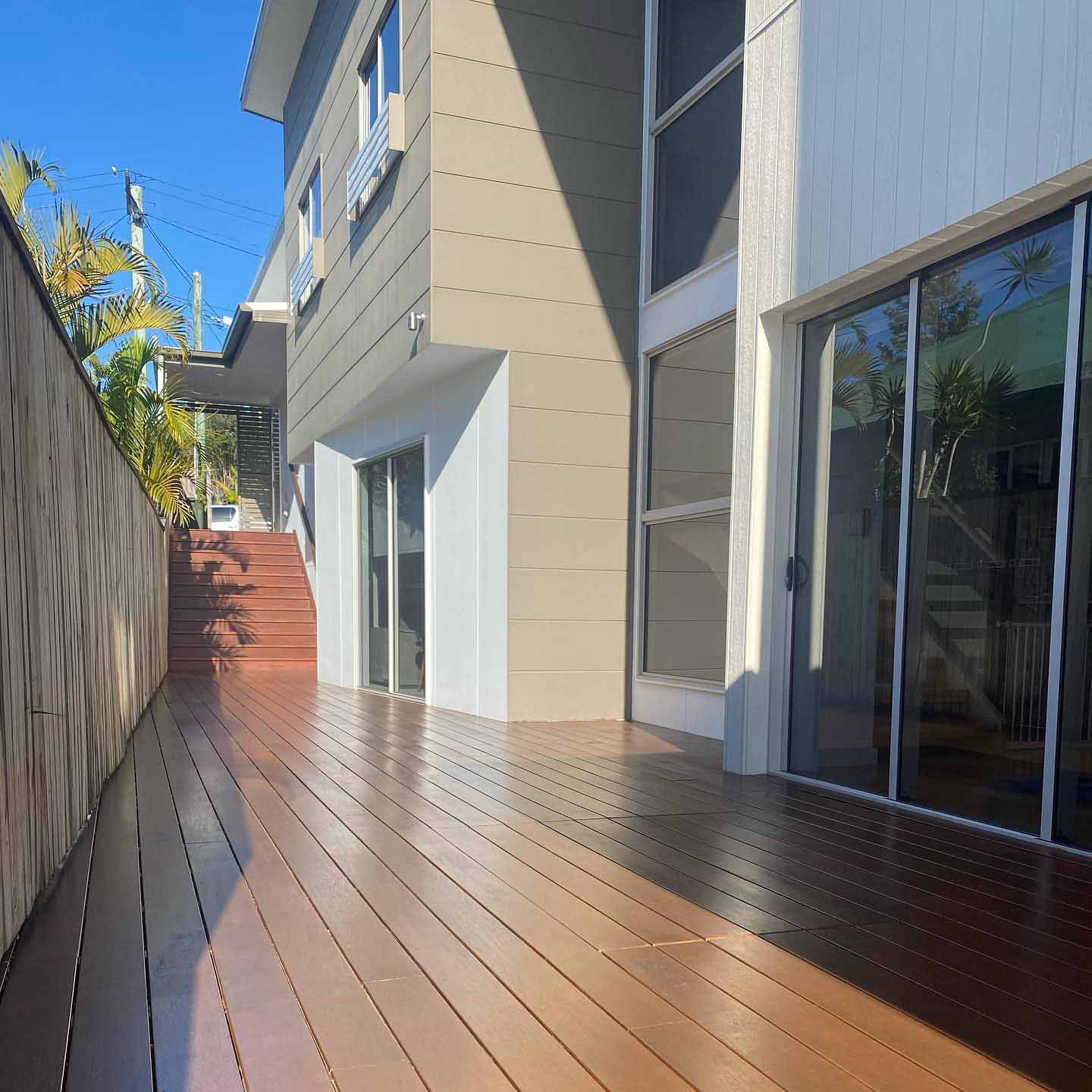Oiled timber side deck with timber steps between a fence and a two-storey house