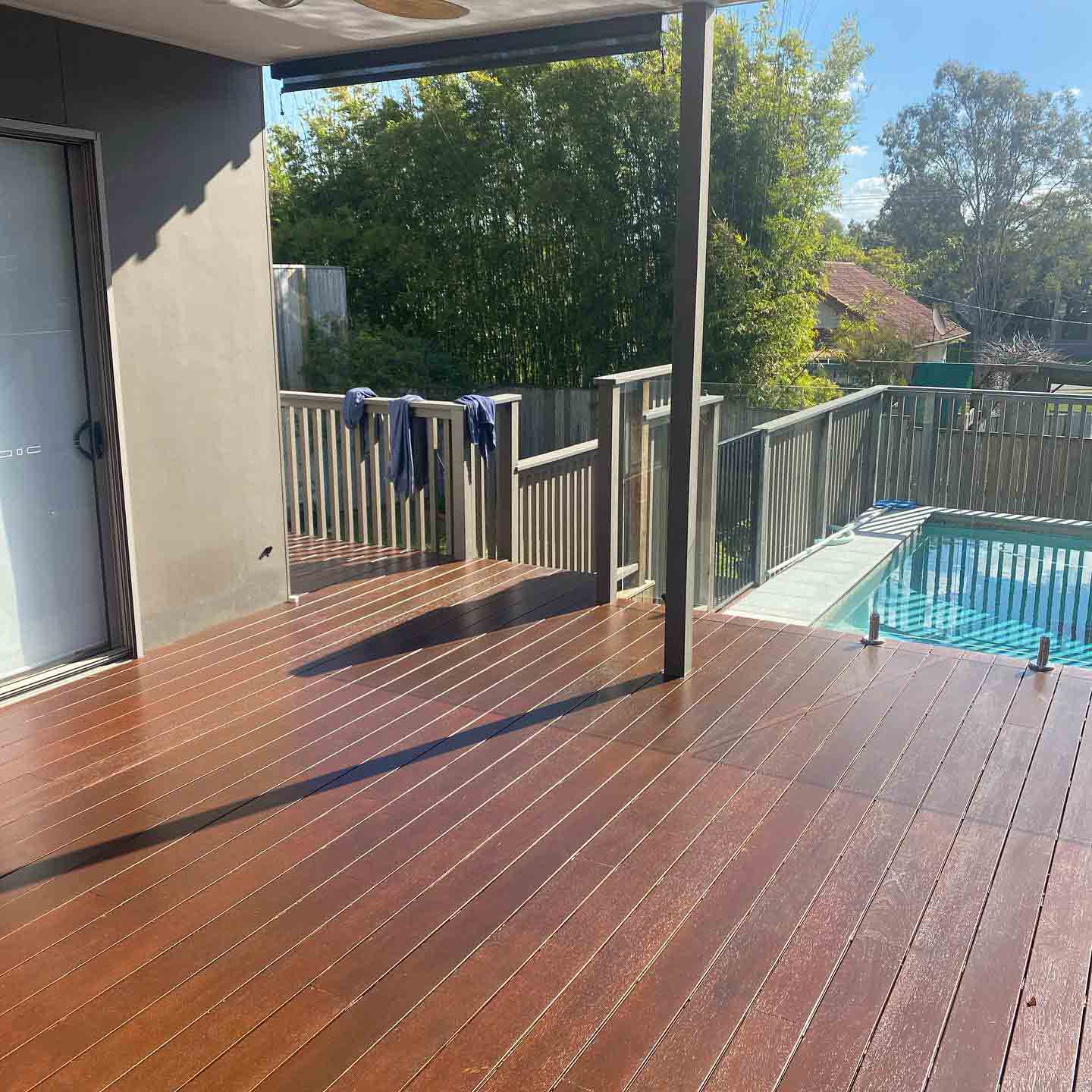 Oiled timber deck under a patio with grey balustrade beside a pool