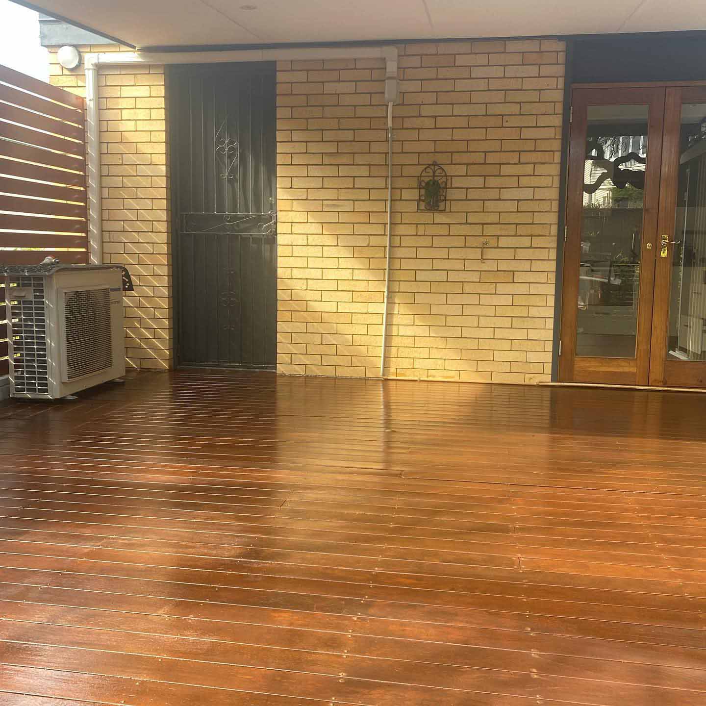 Oiled timber deck under a patio against a cream brick wall