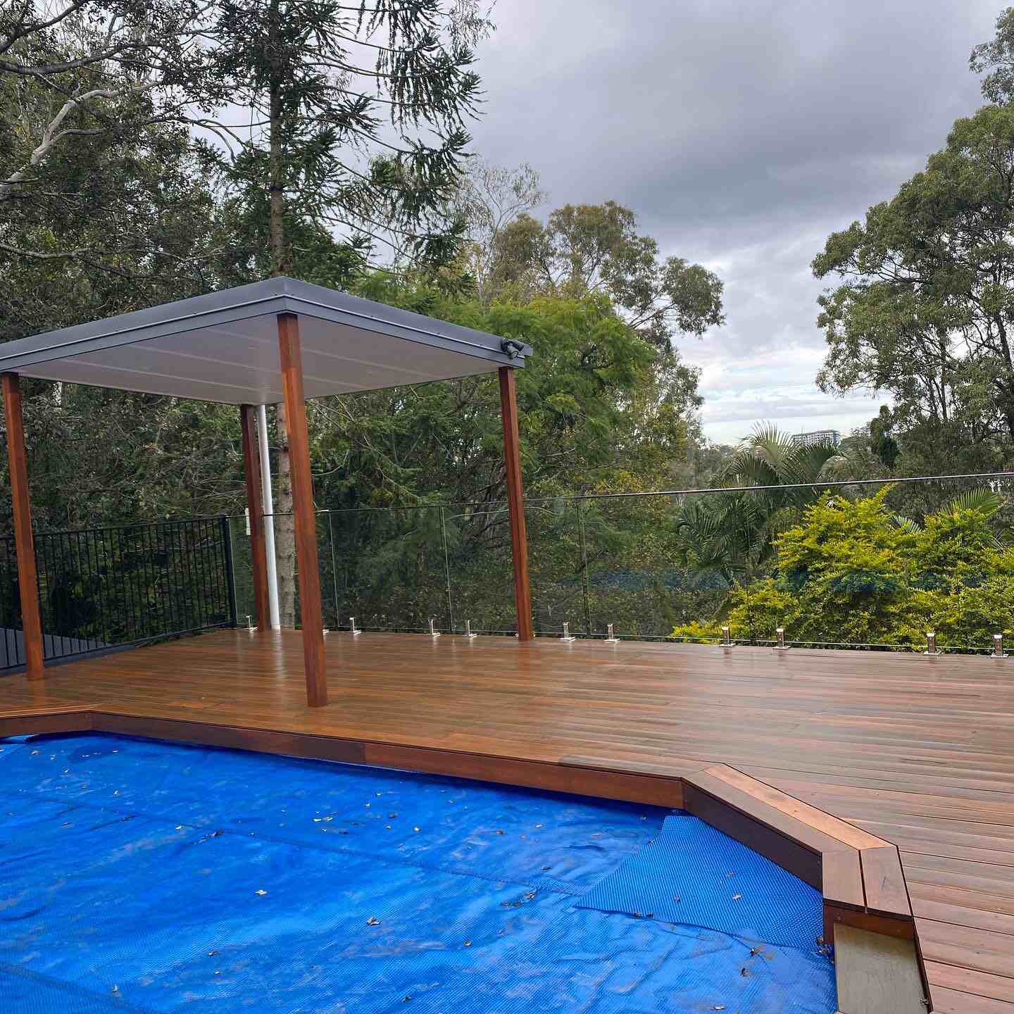 Timber deck with a pavilion beside a pool under a blue cover