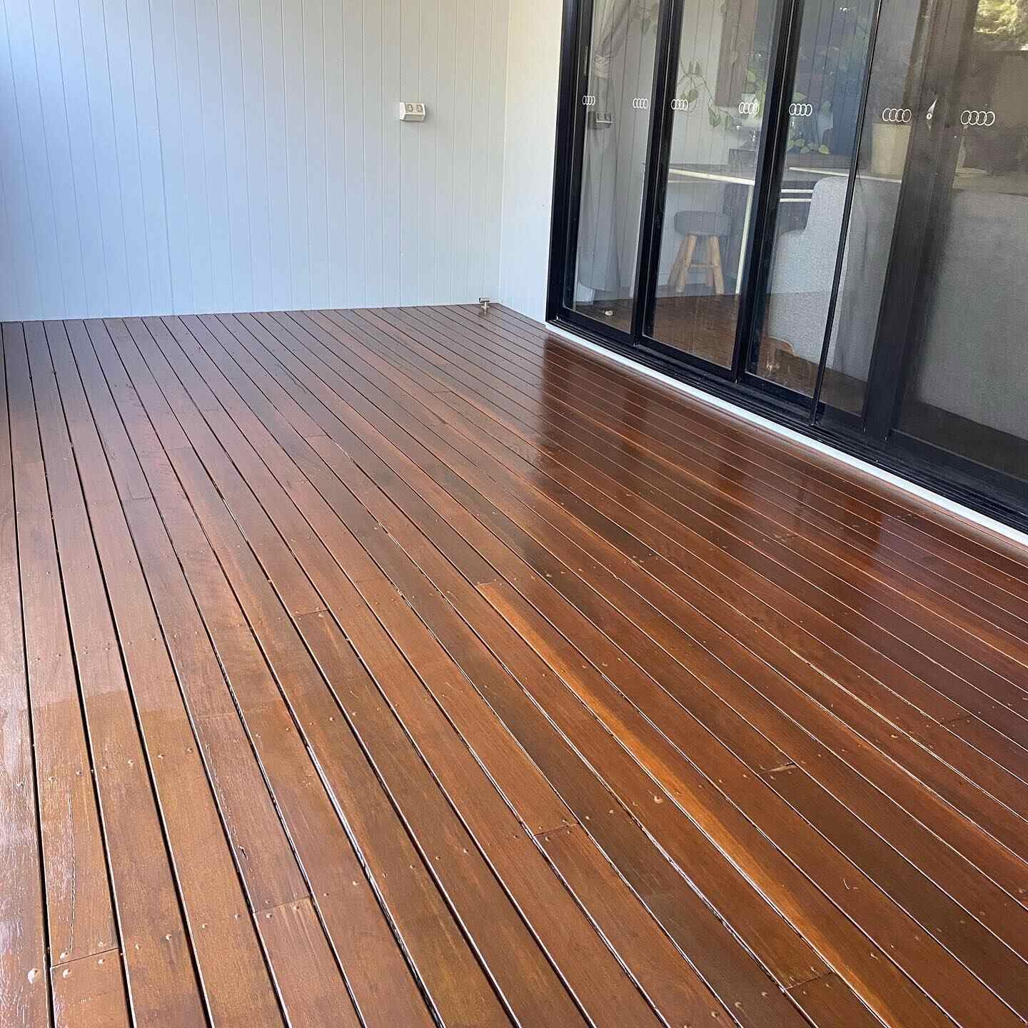 Glossy oiled timber deck beside black-framed sliding doors