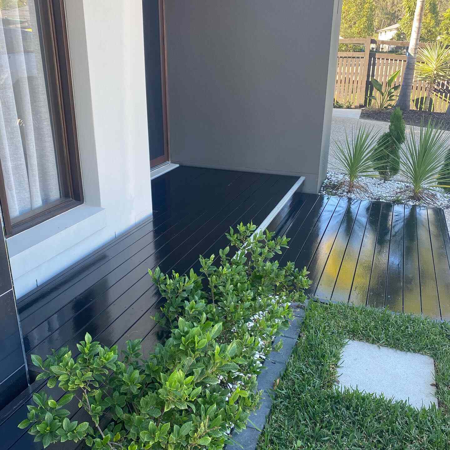 Black-stained deck beside a rendered house with a hedge and lawn