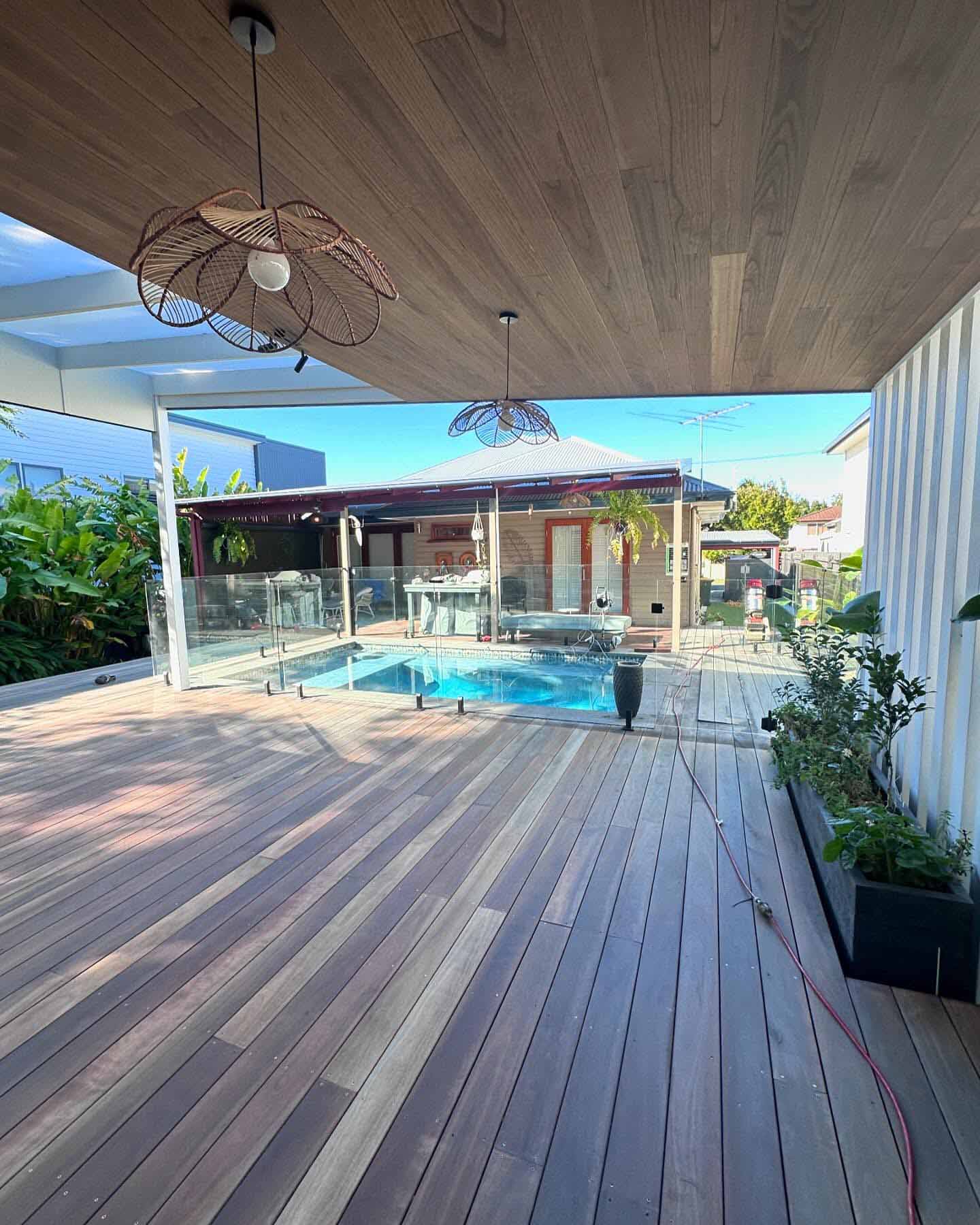 Sanded covered timber deck with pendant lights, looking out to a glass-fenced pool