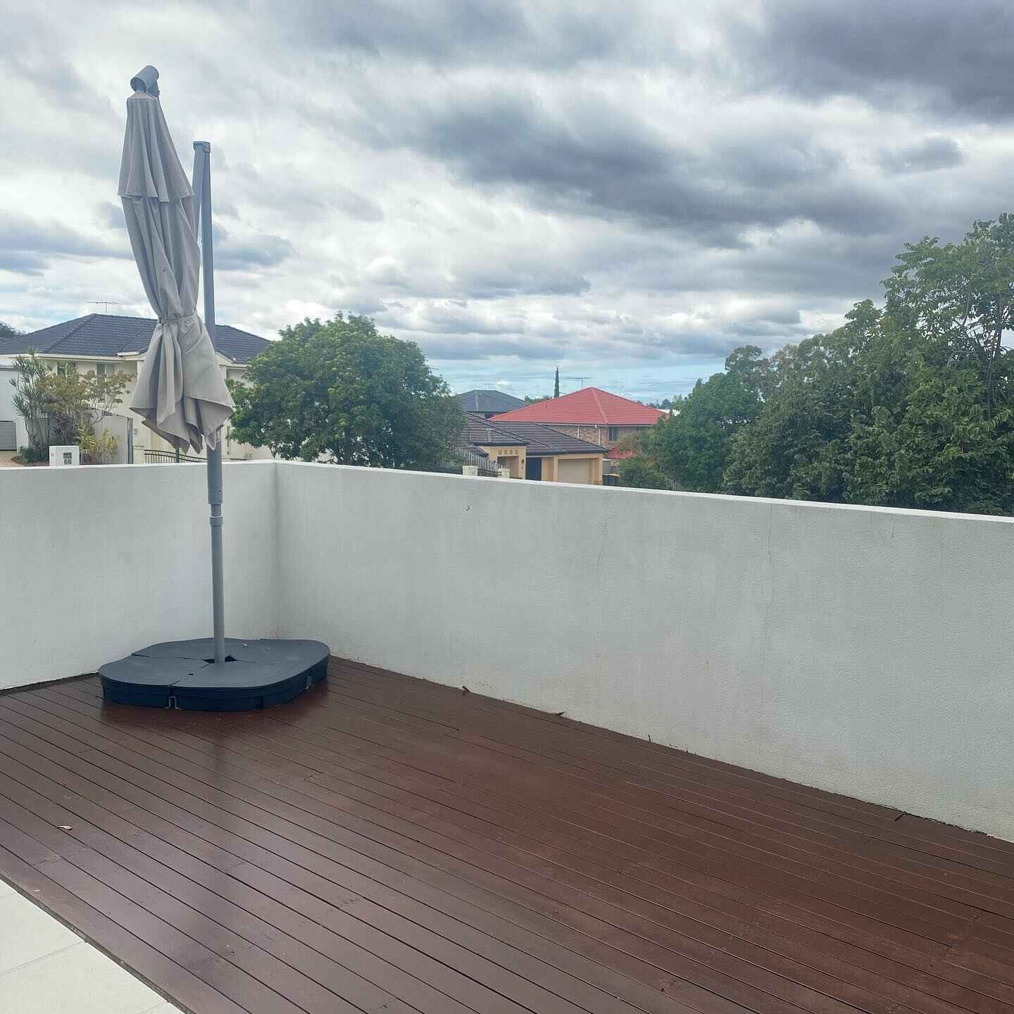 Dark oiled timber balcony deck with a rendered wall and an umbrella