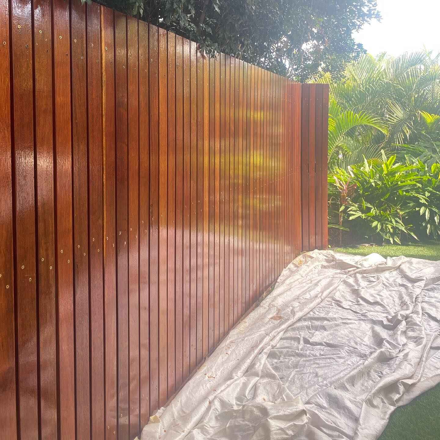 Freshly oiled vertical timber batten fence with a drop sheet below