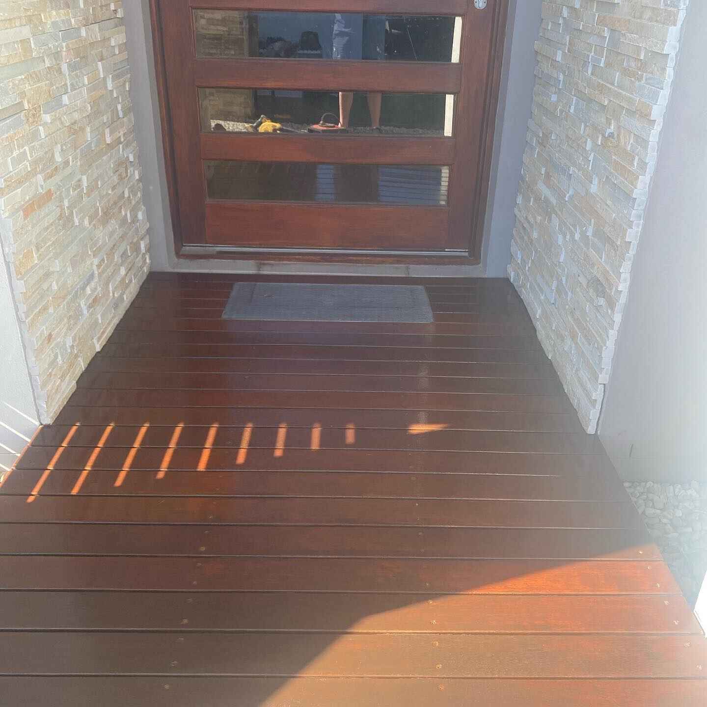 Oiled timber entry deck between stone-clad walls at a timber front door