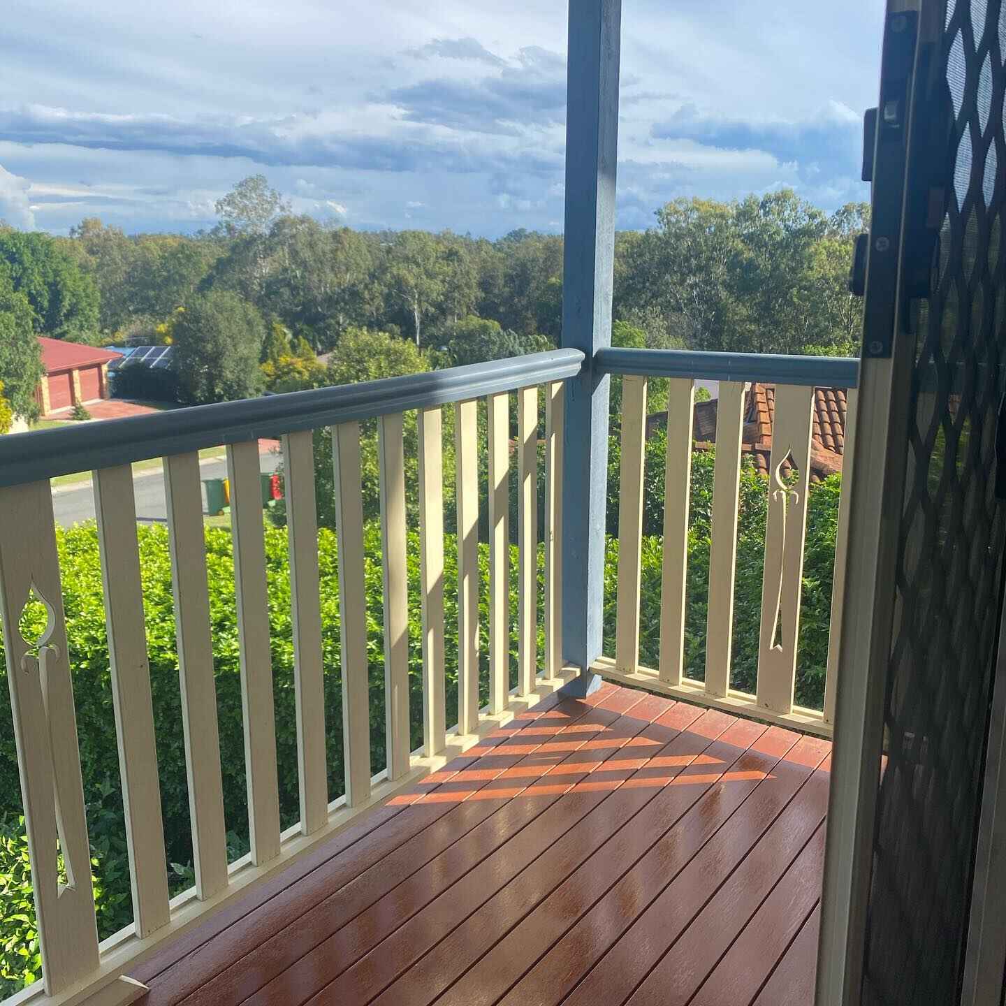 Oiled timber verandah corner with white timber balustrade overlooking treetops