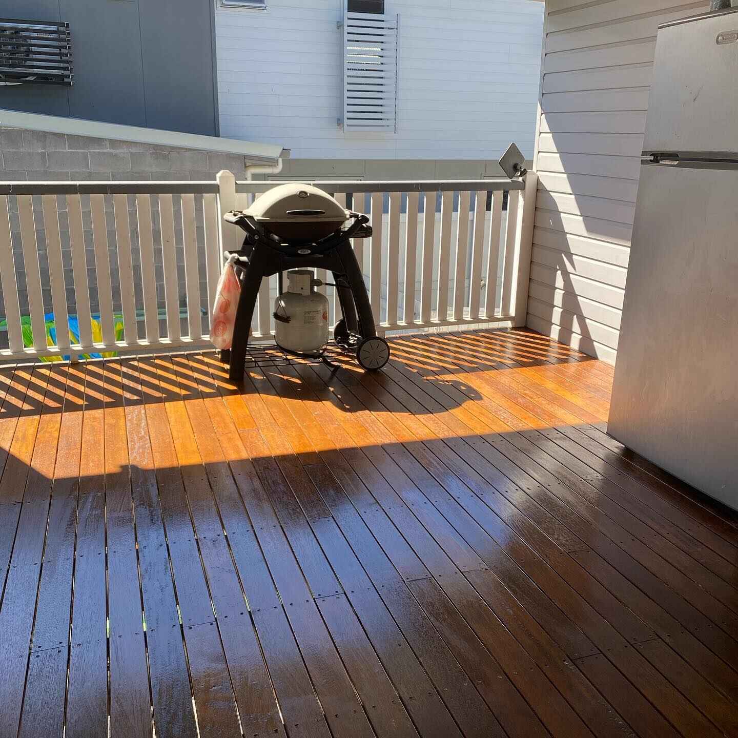 Sunlit oiled timber deck with white balustrade and a kettle barbecue