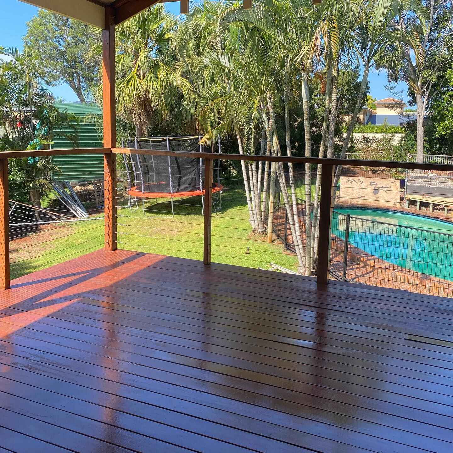 Oiled timber deck with timber and wire balustrade overlooking a pool and trampoline
