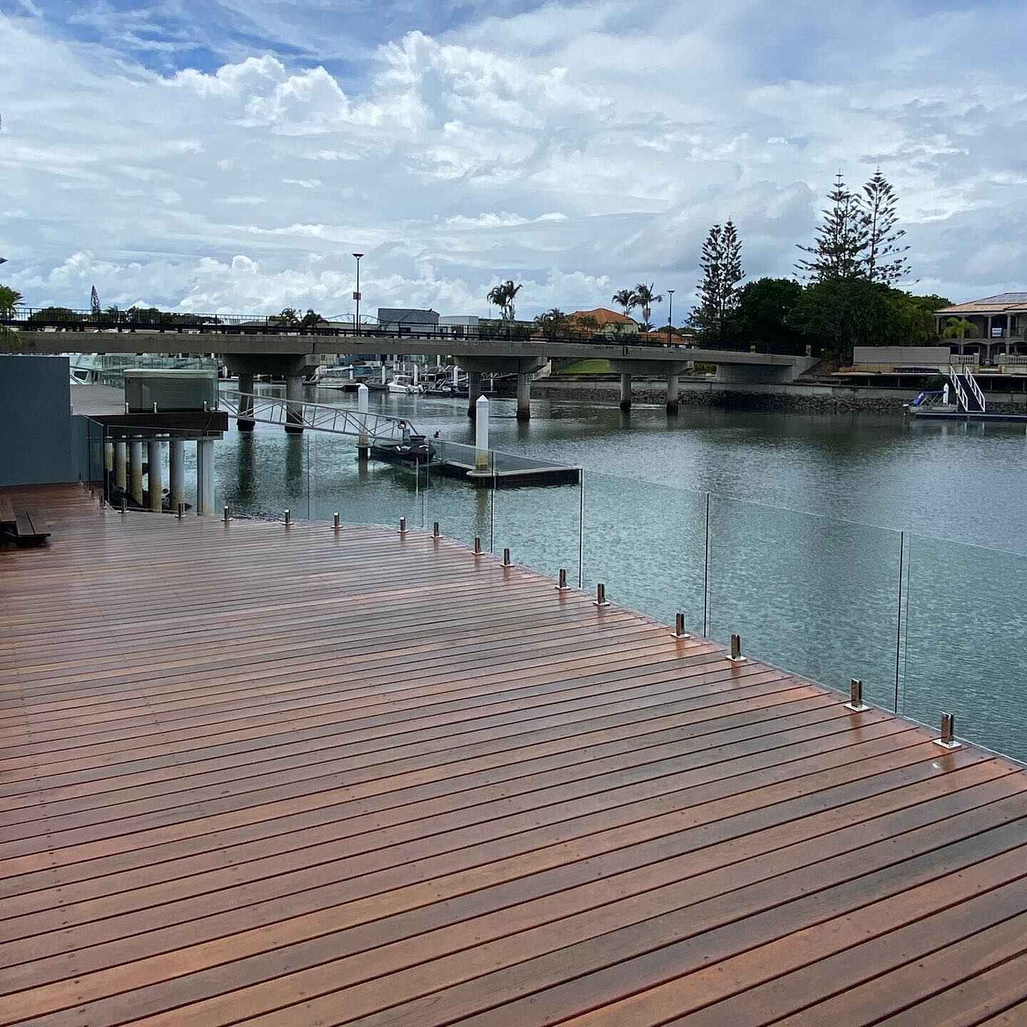 Waterfront timber deck with glass balustrade overlooking a canal and bridge