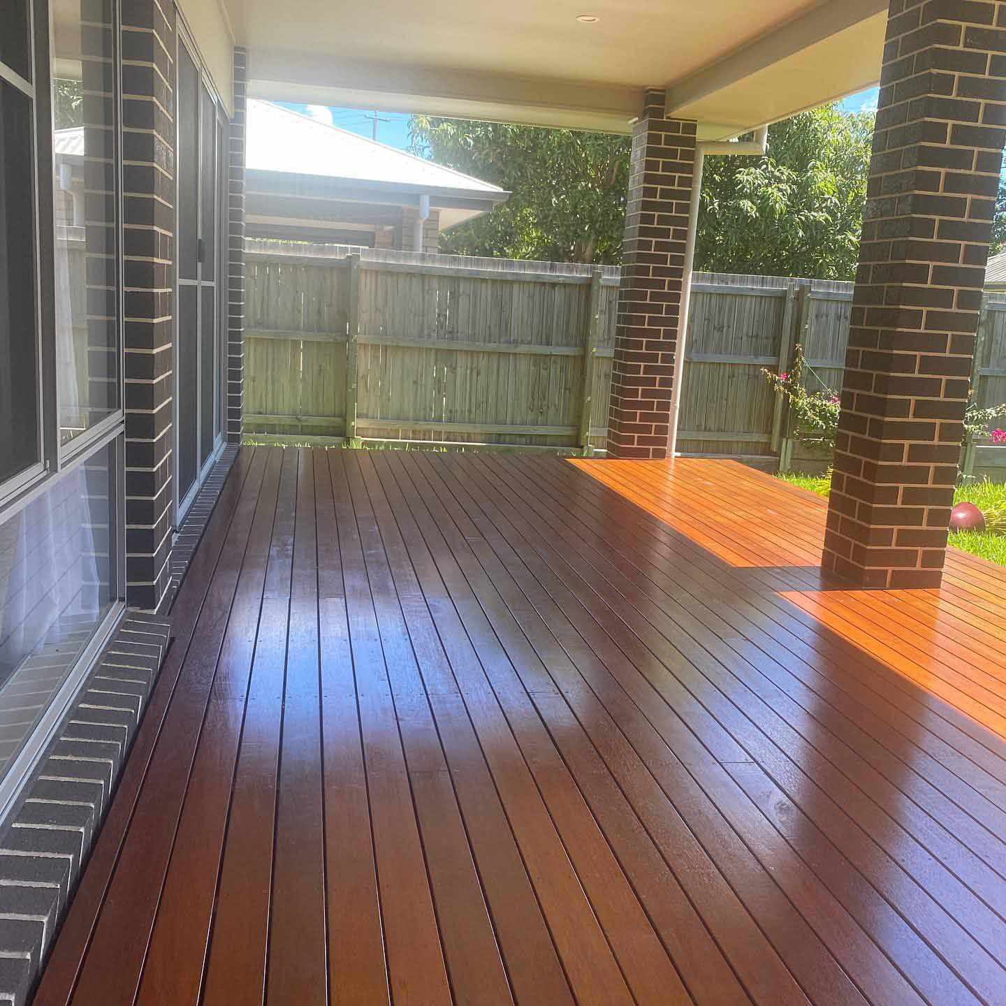 Glossy oiled timber deck under a patio between dark brick pillars