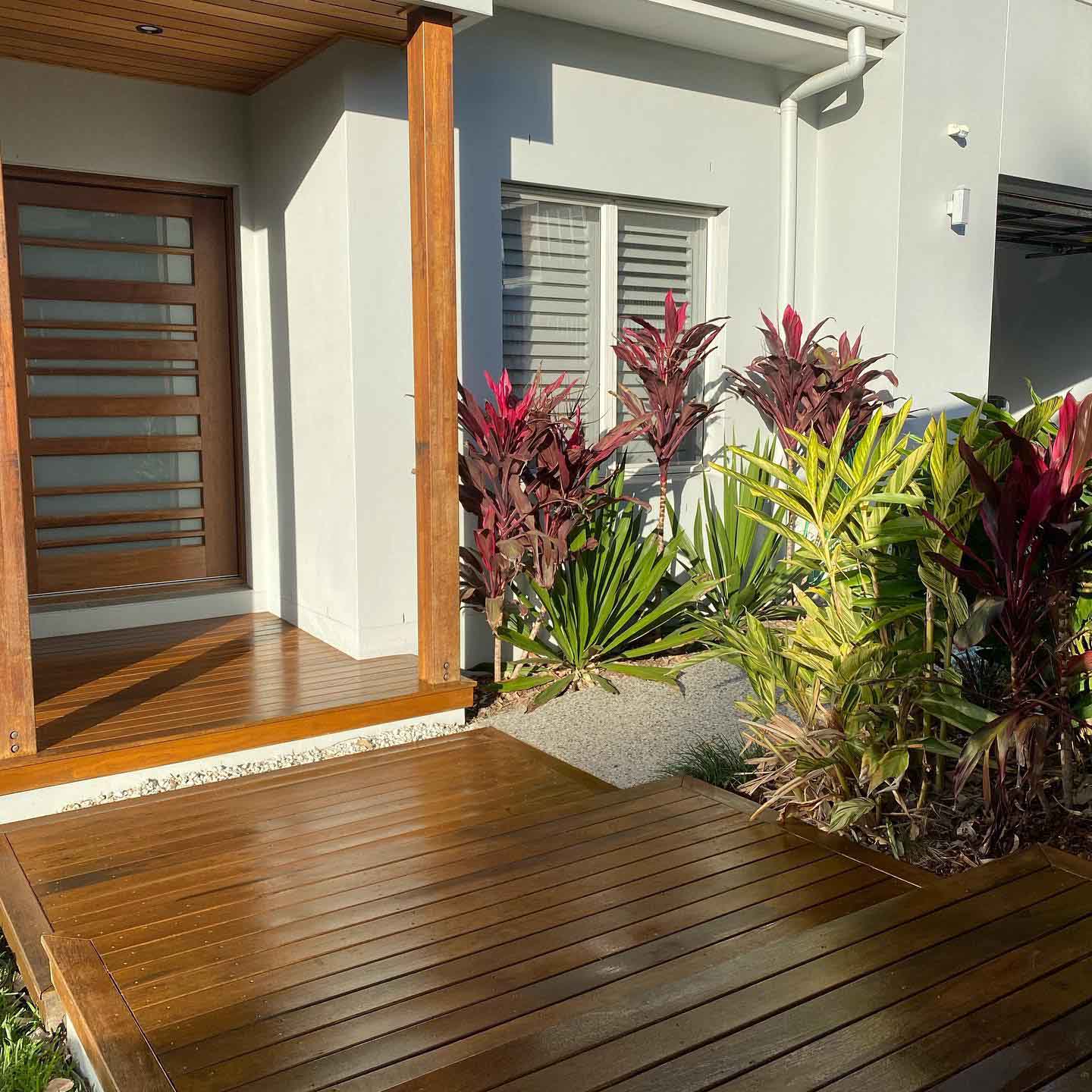Oiled timber entry deck by a timber front door with a tropical garden bed