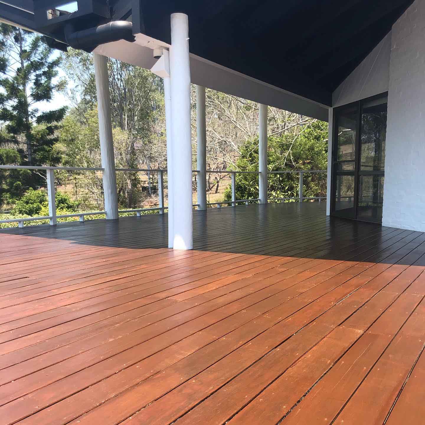 Oiled timber deck under a raked roof with white posts and wire balustrade