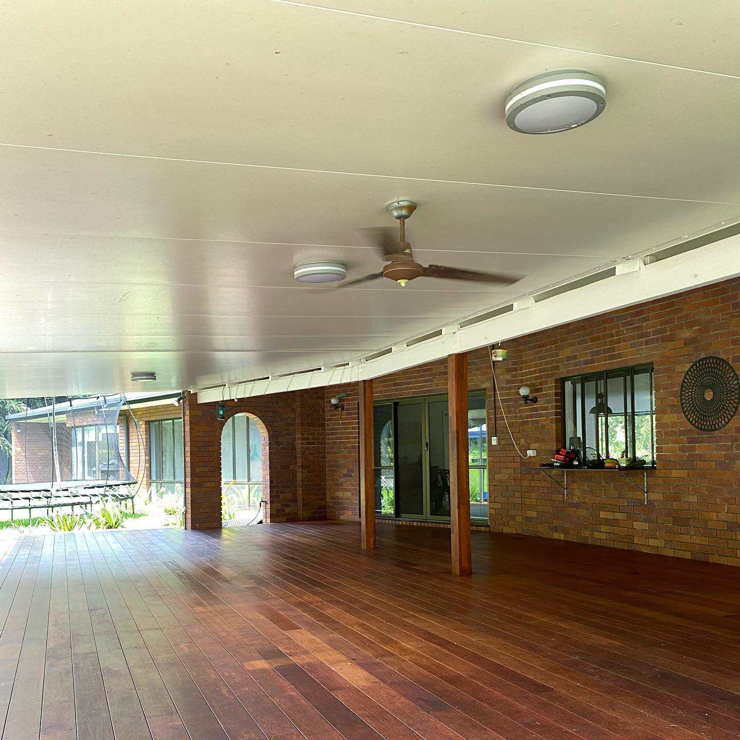 Oiled timber deck under a large patio roof along a brick house