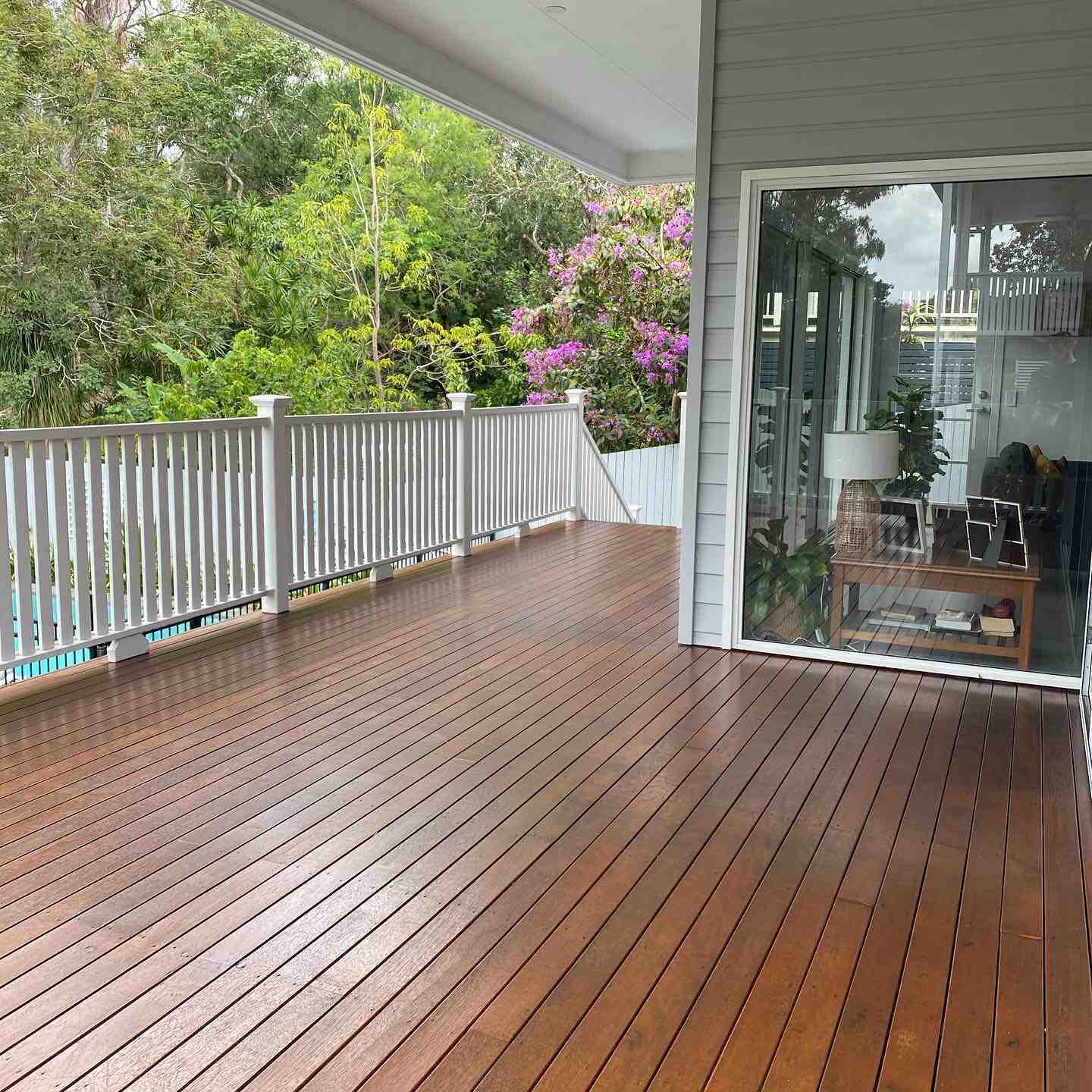 Oiled timber verandah with white timber balustrade beside a glass sliding door