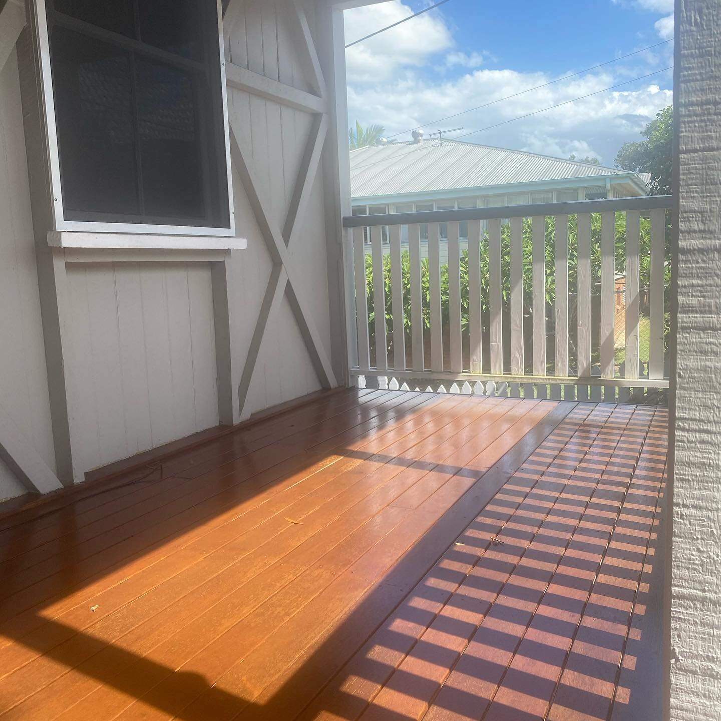 Sunlit oiled timber verandah with white timber balustrade beside weatherboards