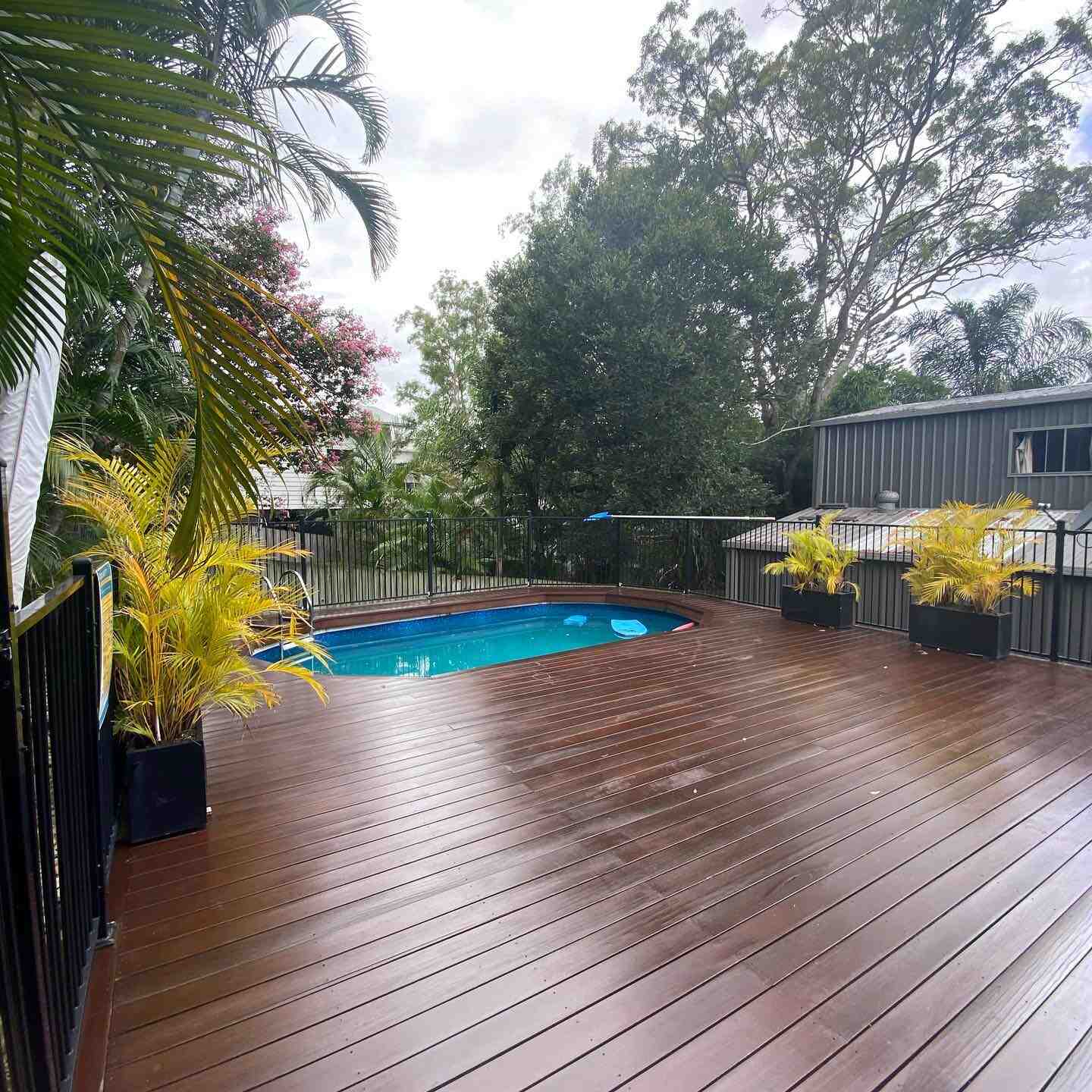 Wet oiled timber deck with black balustrade beside an above-ground pool