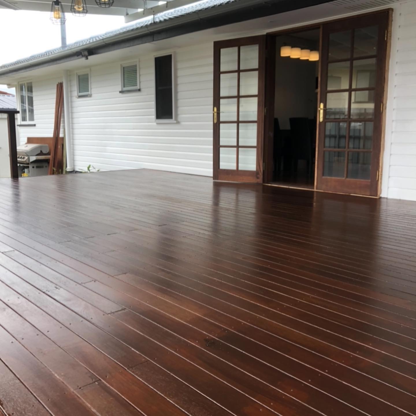 Glossy oiled timber deck outside timber French doors on a white weatherboard house