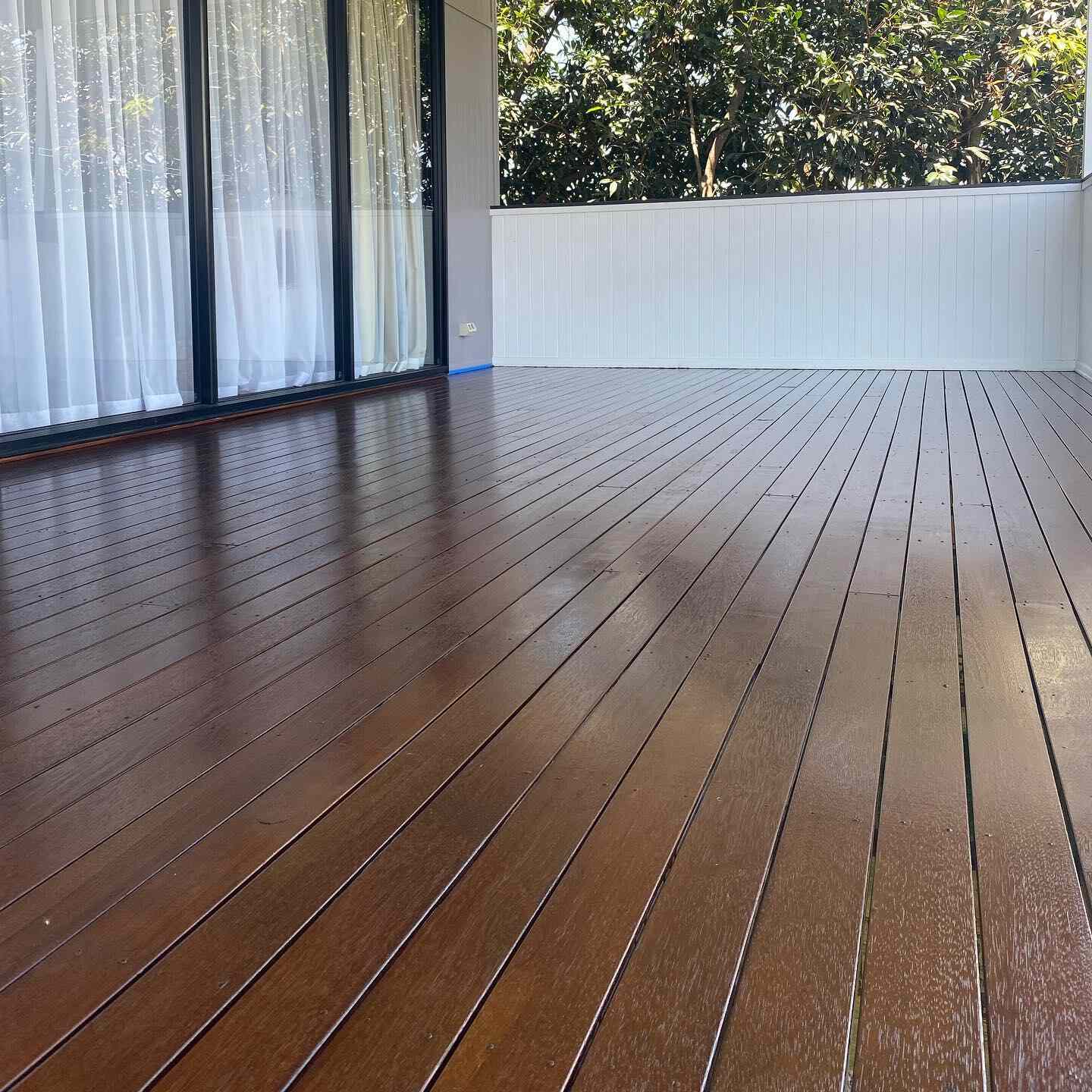 Glossy oiled timber deck beside floor-to-ceiling sliding doors and a white wall