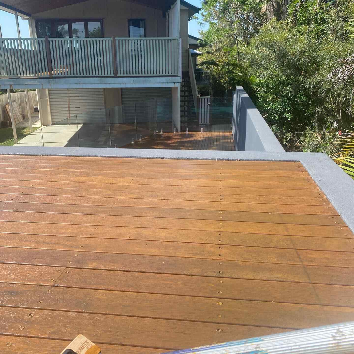 Freshly oiled timber deck with a rendered edge, below a two-storey house