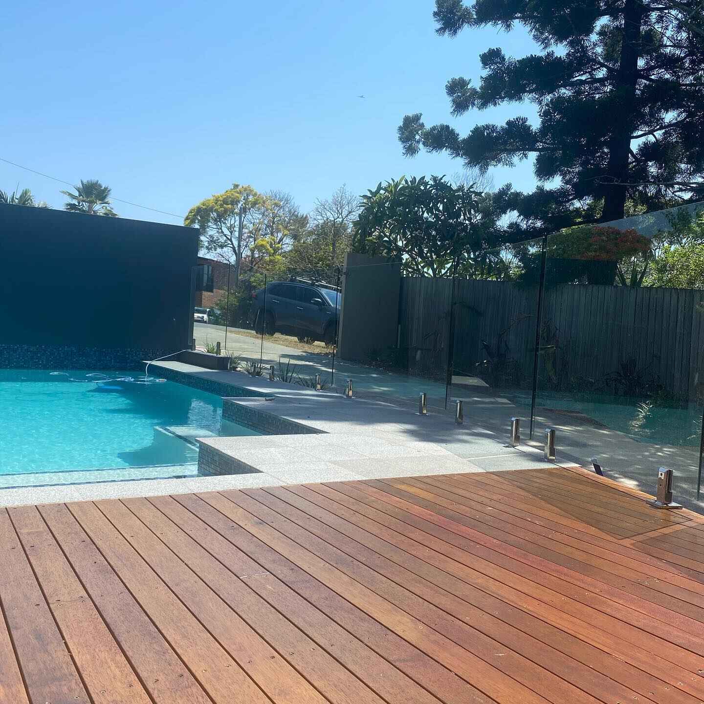 Oiled timber deck beside a pool with glass fencing and paving