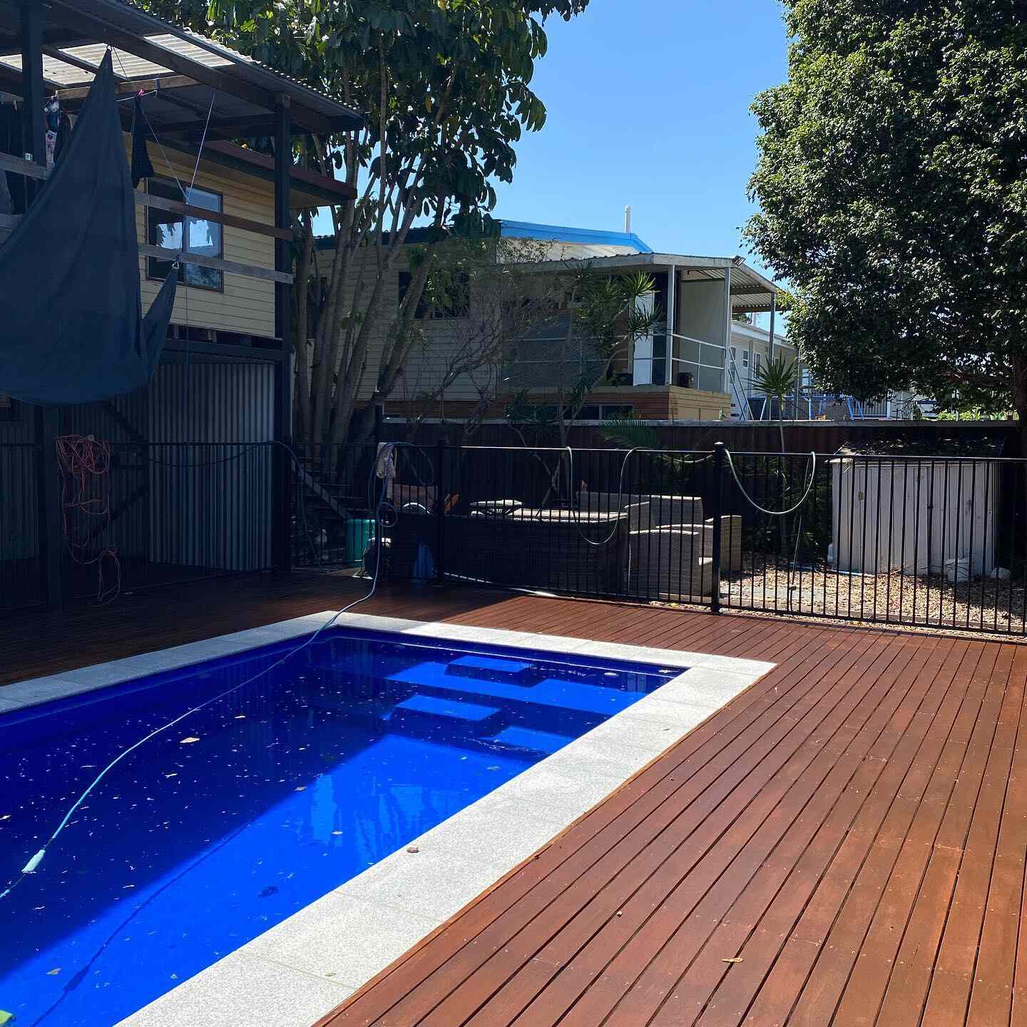 Oiled timber deck around a blue-tiled pool with pool fencing