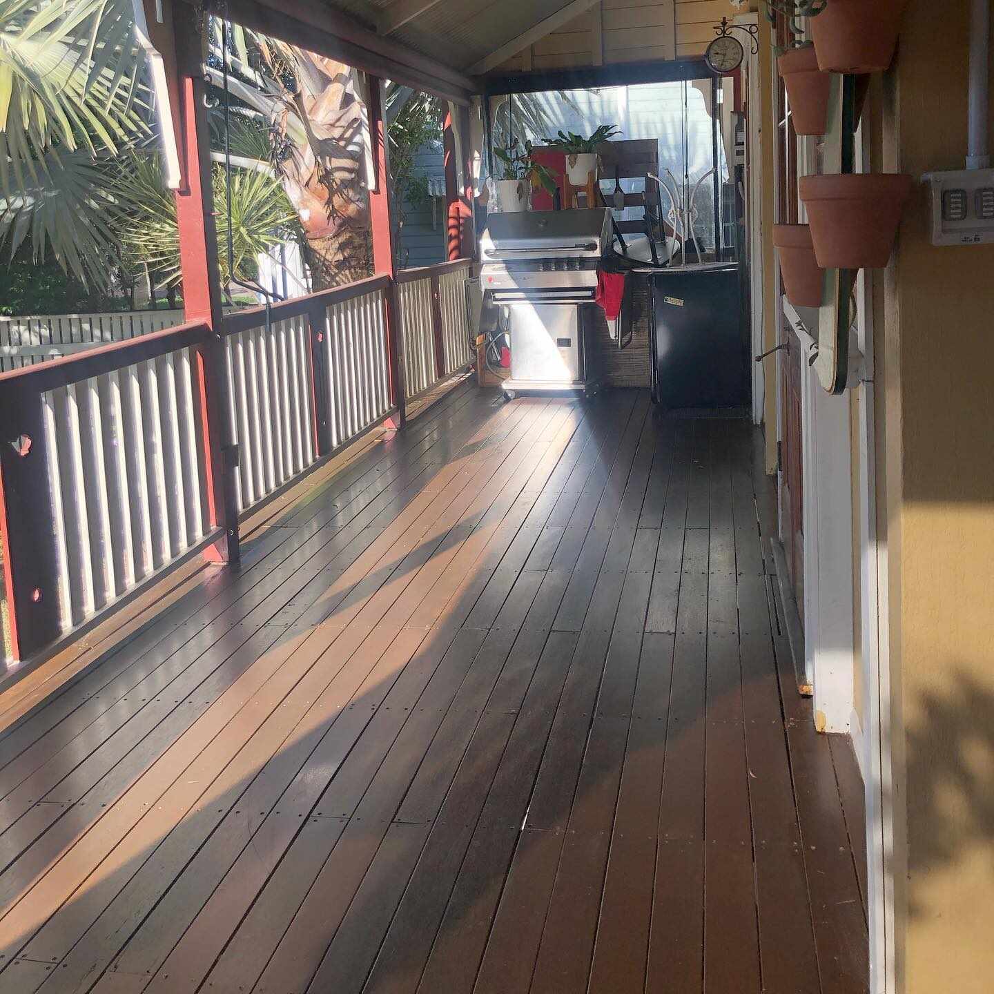 Long dark timber verandah with red and white balustrade and hanging pots