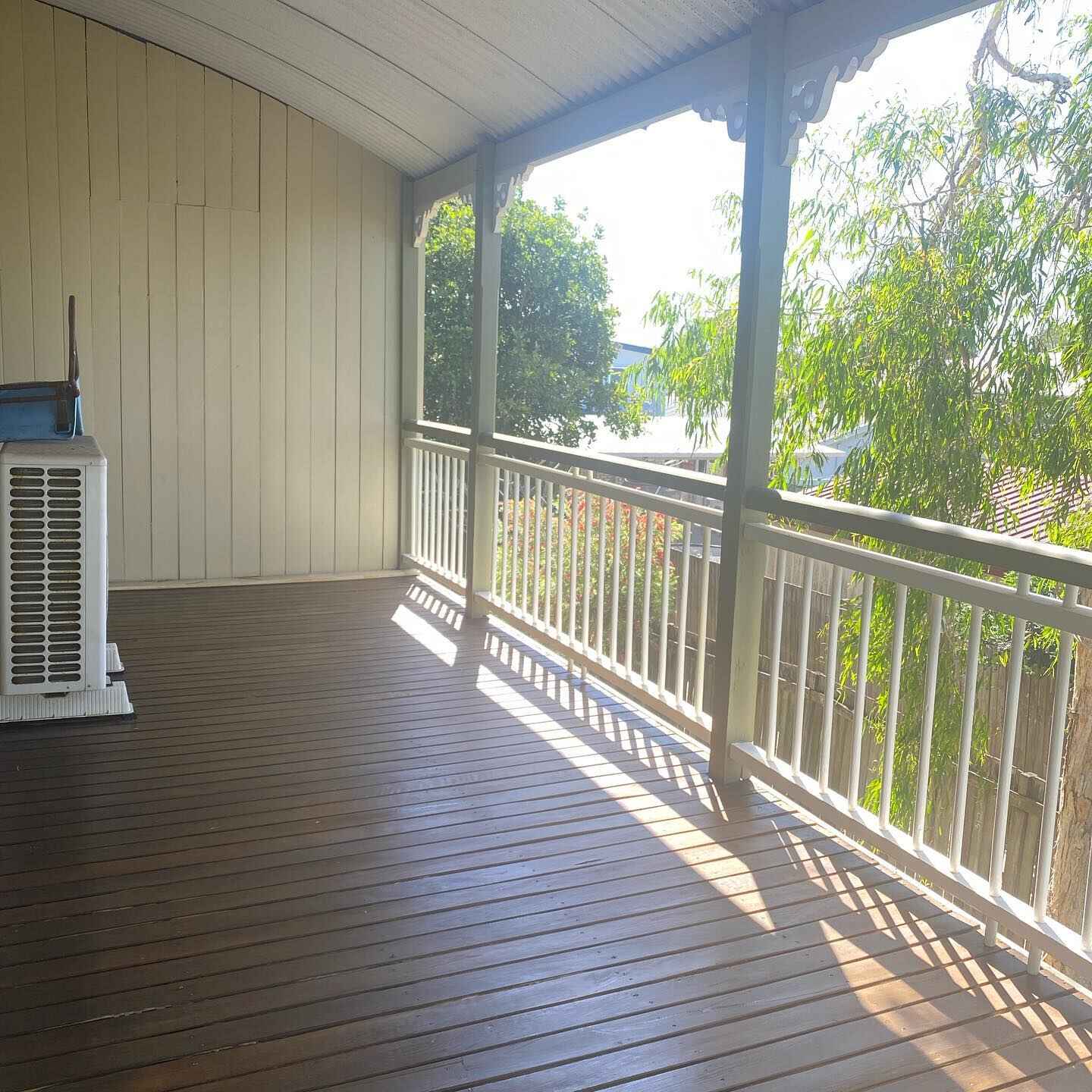 Oiled timber verandah with white balustrade beside cream weatherboards