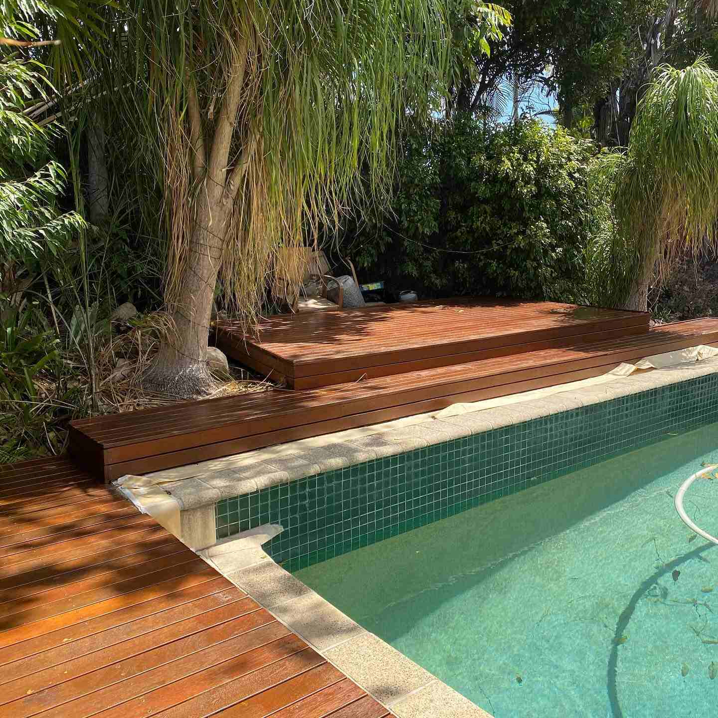 Timber deck and steps around a green-tiled pool among palms