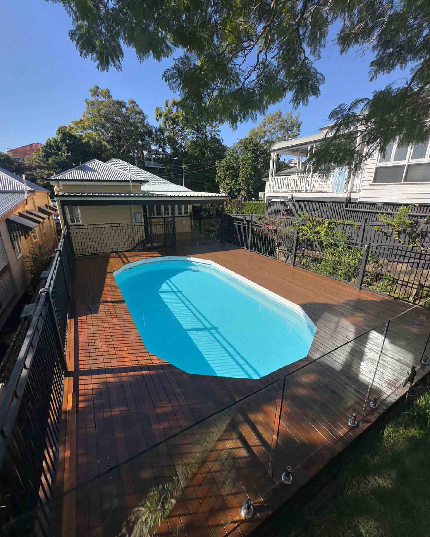 Timber deck around an oval fibreglass pool with glass fencing, seen from above