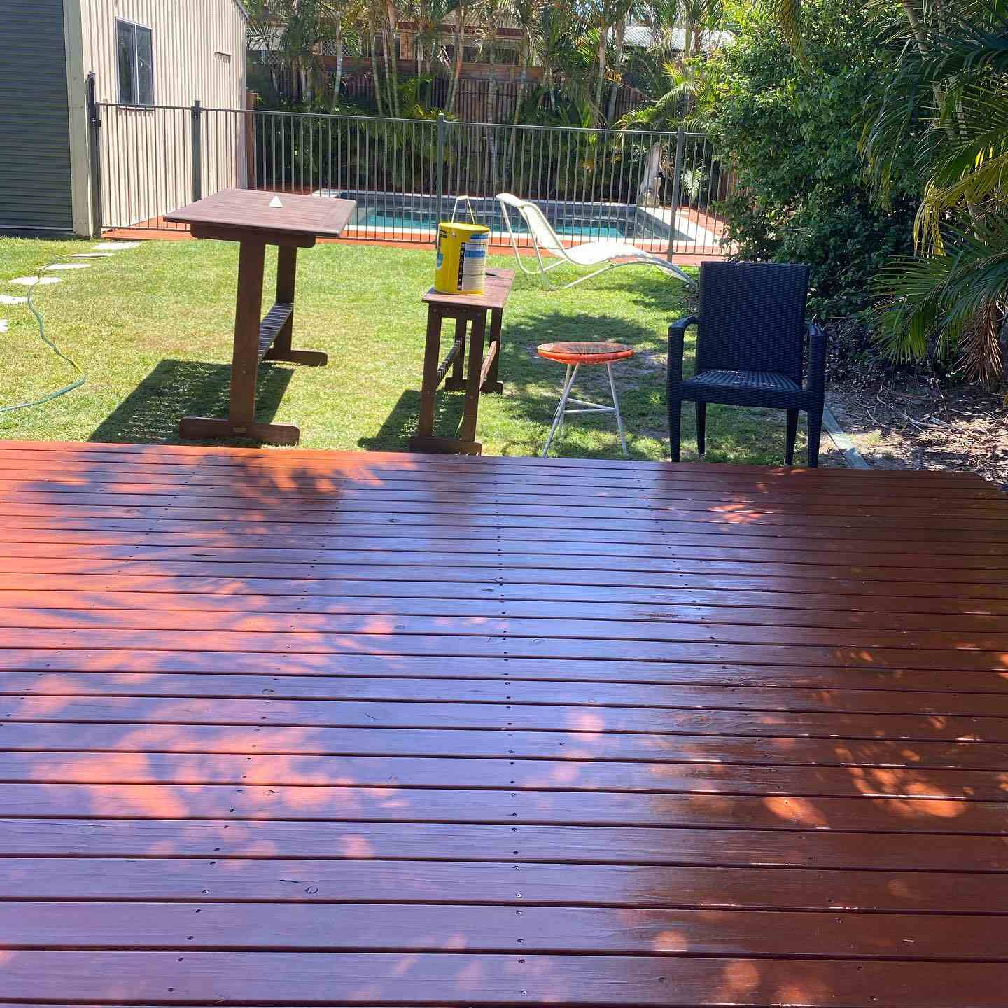 Glossy oiled timber deck with dappled shade beside a lawn and outdoor table