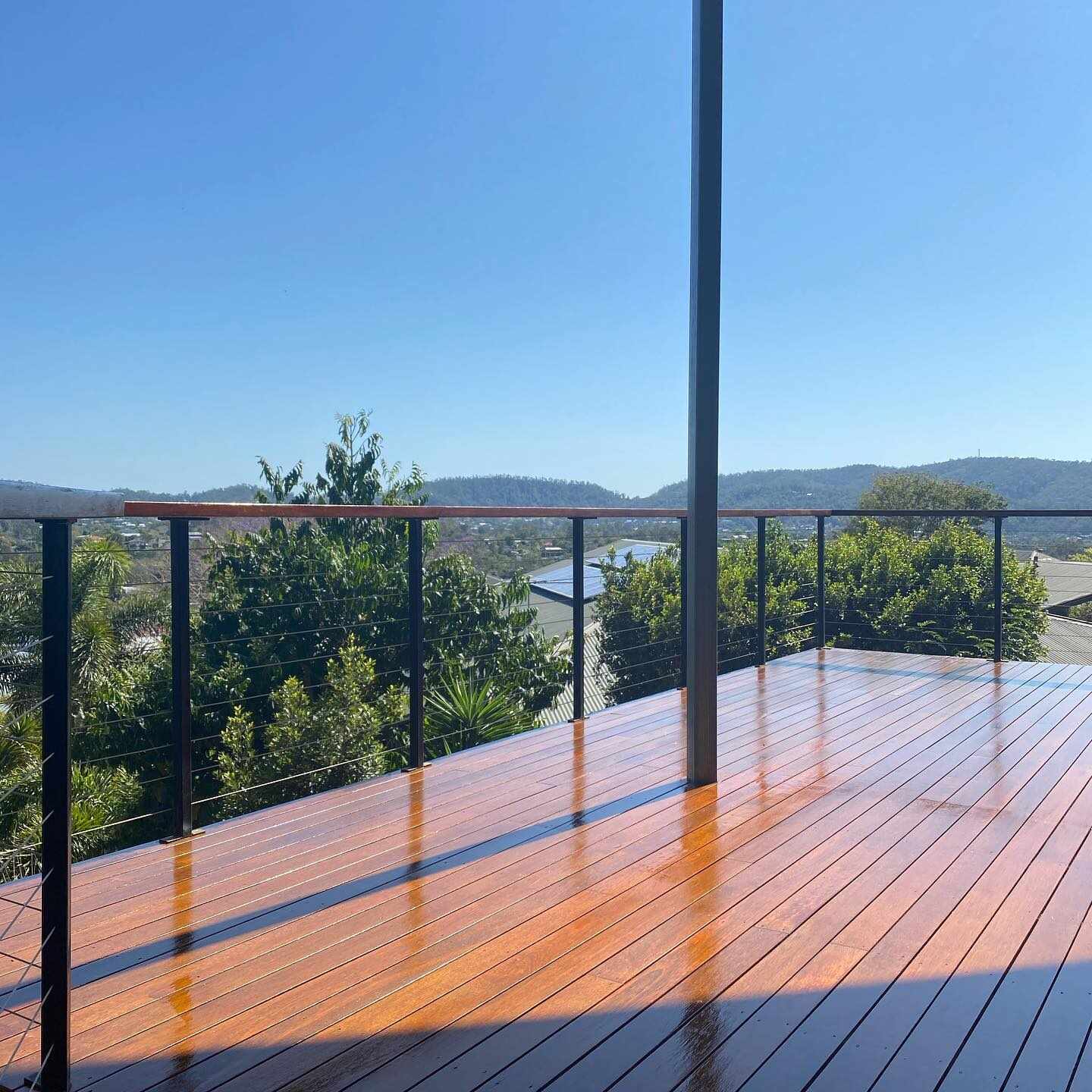 Oiled timber deck with black wire balustrade overlooking hills