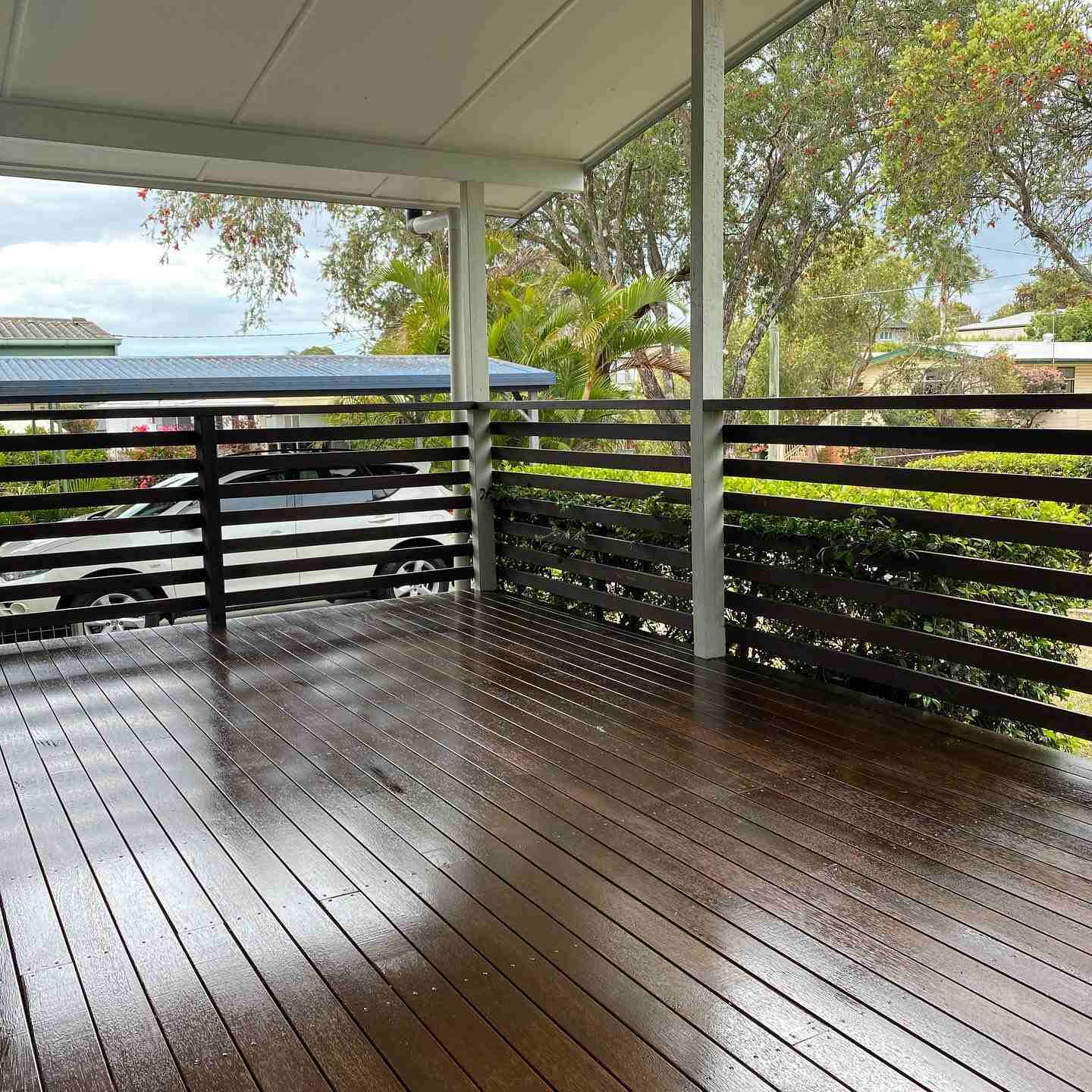 Wet oiled timber deck with dark horizontal slat balustrade under a roof