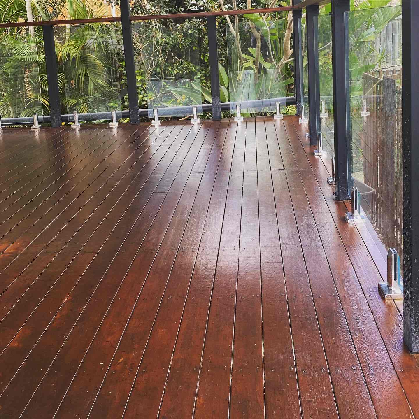 Glossy oiled timber deck with glass balustrade among tropical plants