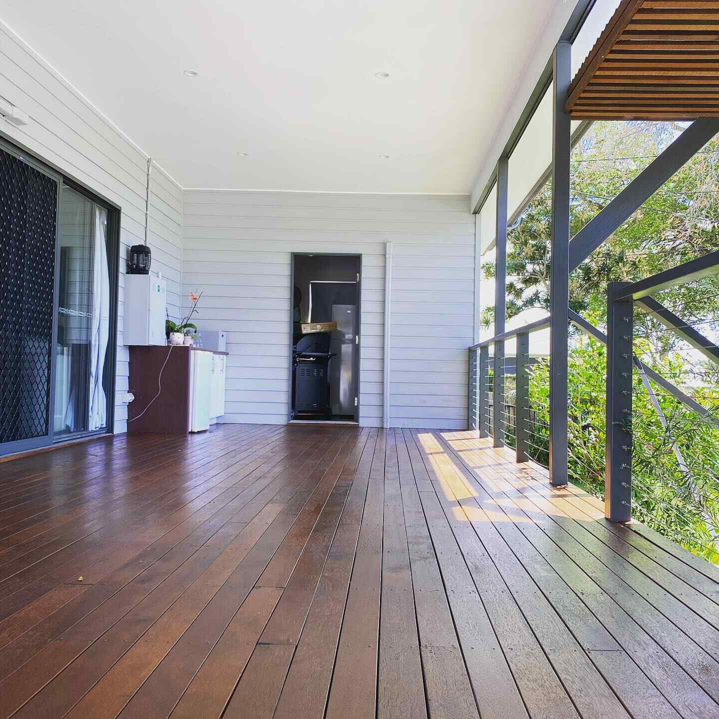 Oiled timber balcony along a white weatherboard house with steel balustrade