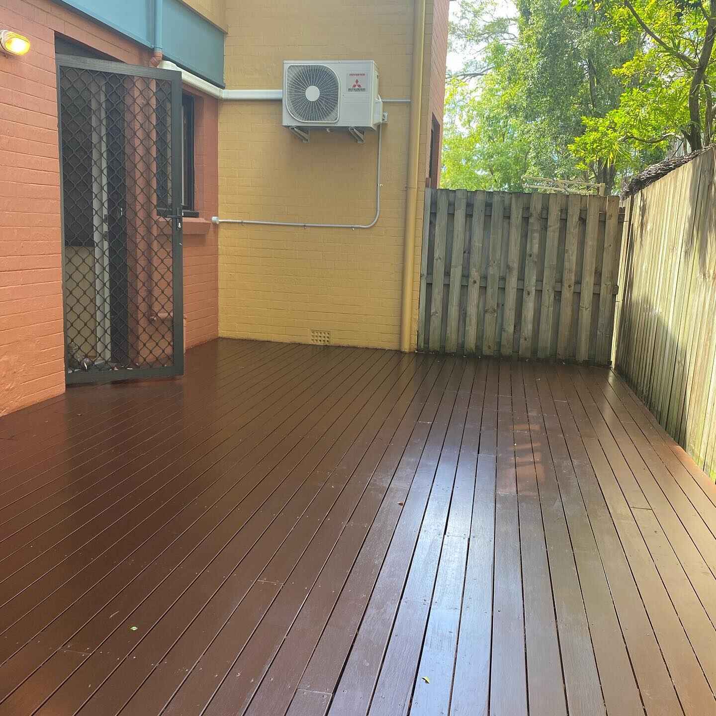 Glossy oiled timber courtyard deck by a brick house and timber fence