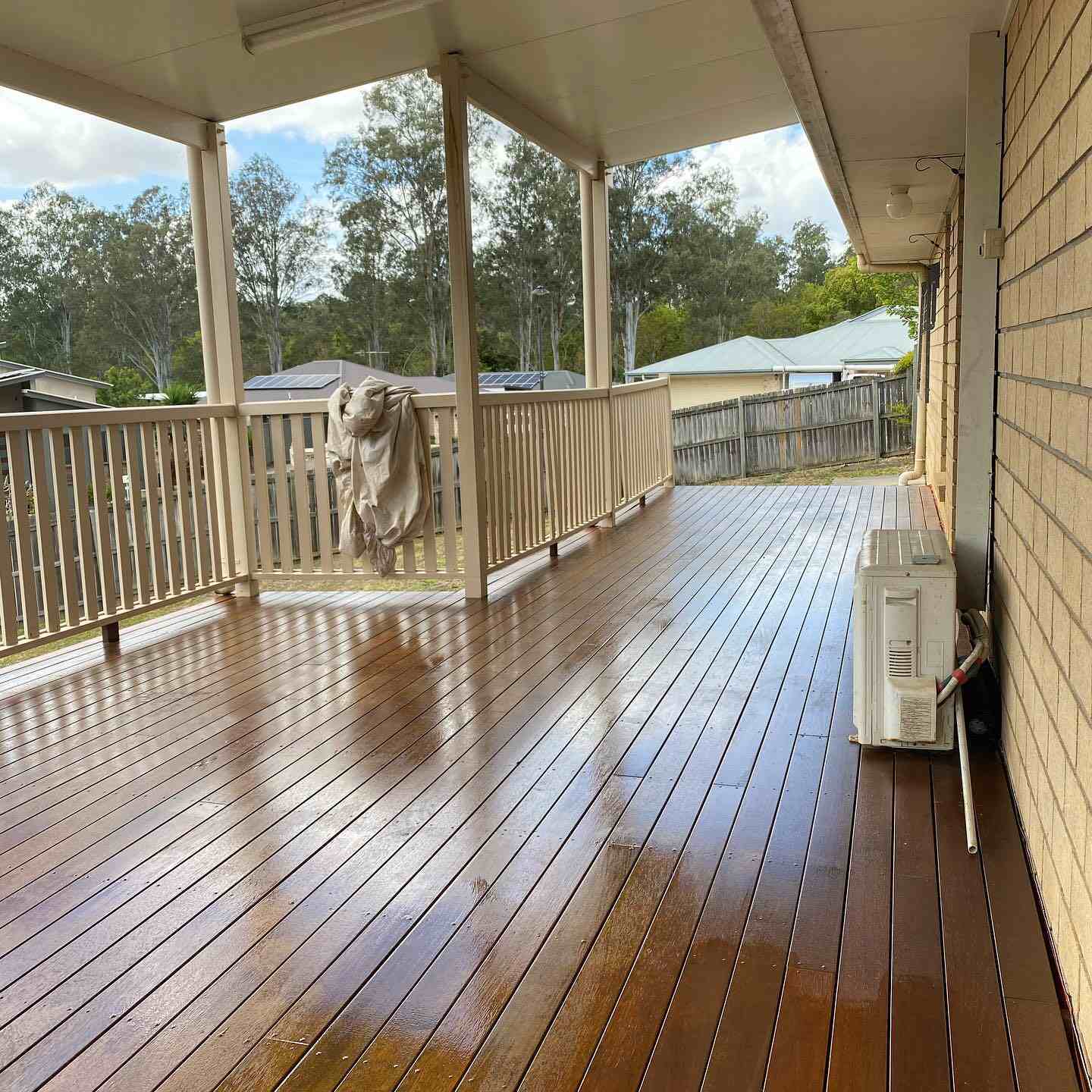 Glossy wet oiled timber verandah with timber balustrade along a brick wall