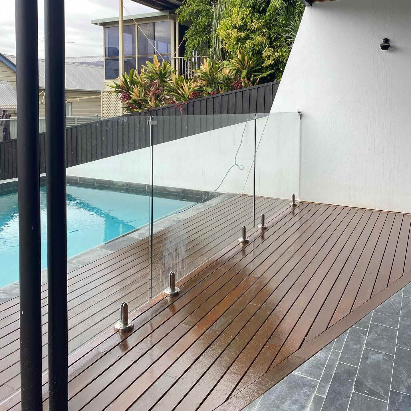 Oiled timber pool deck with glass fencing beside a slate-tiled area