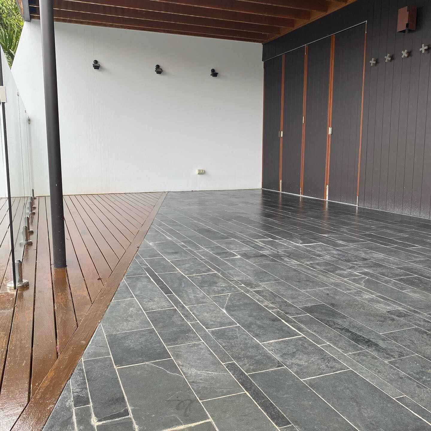 Oiled timber deck strip beside dark slate tiles under a covered area