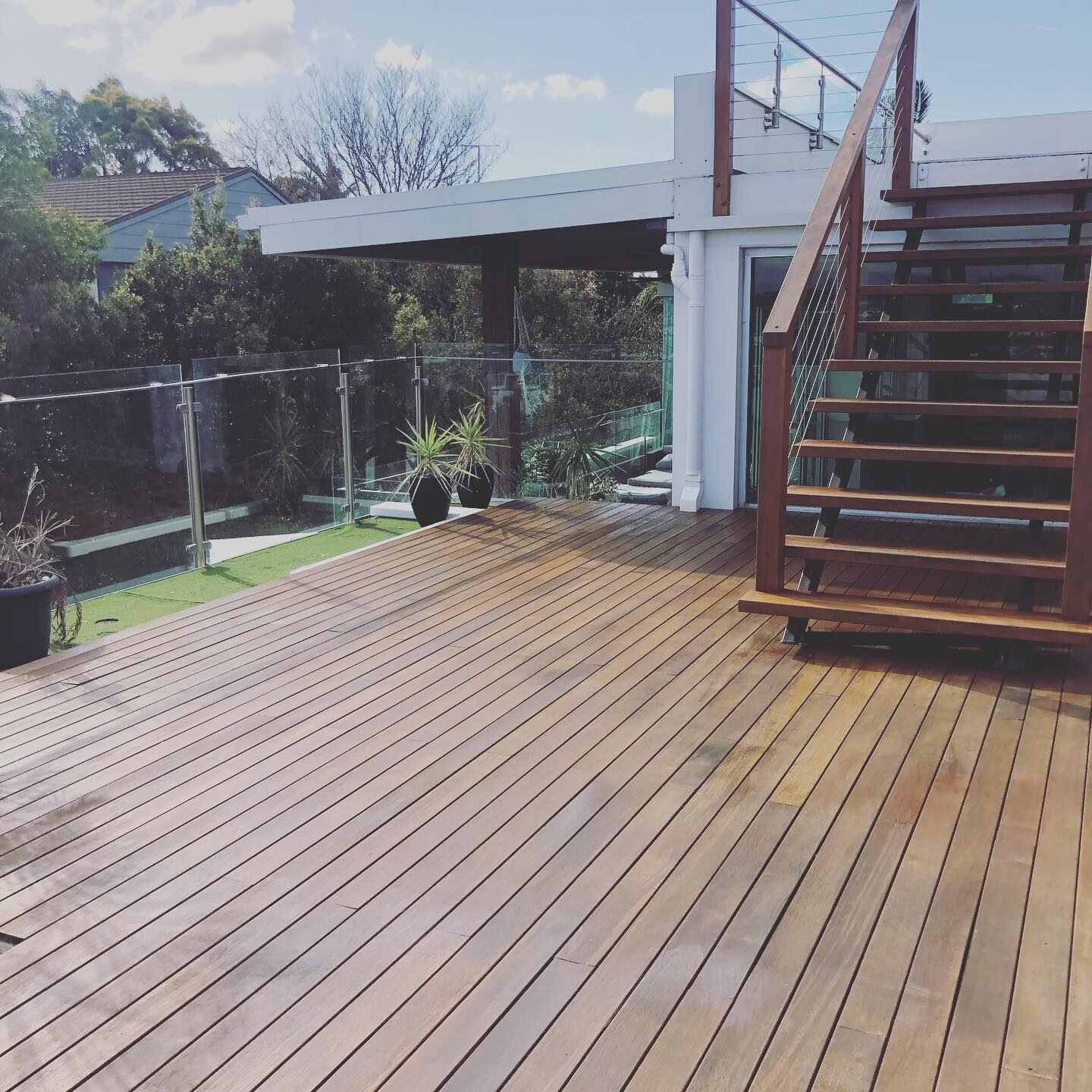 Oiled timber deck at the foot of timber stairs with glass balustrade