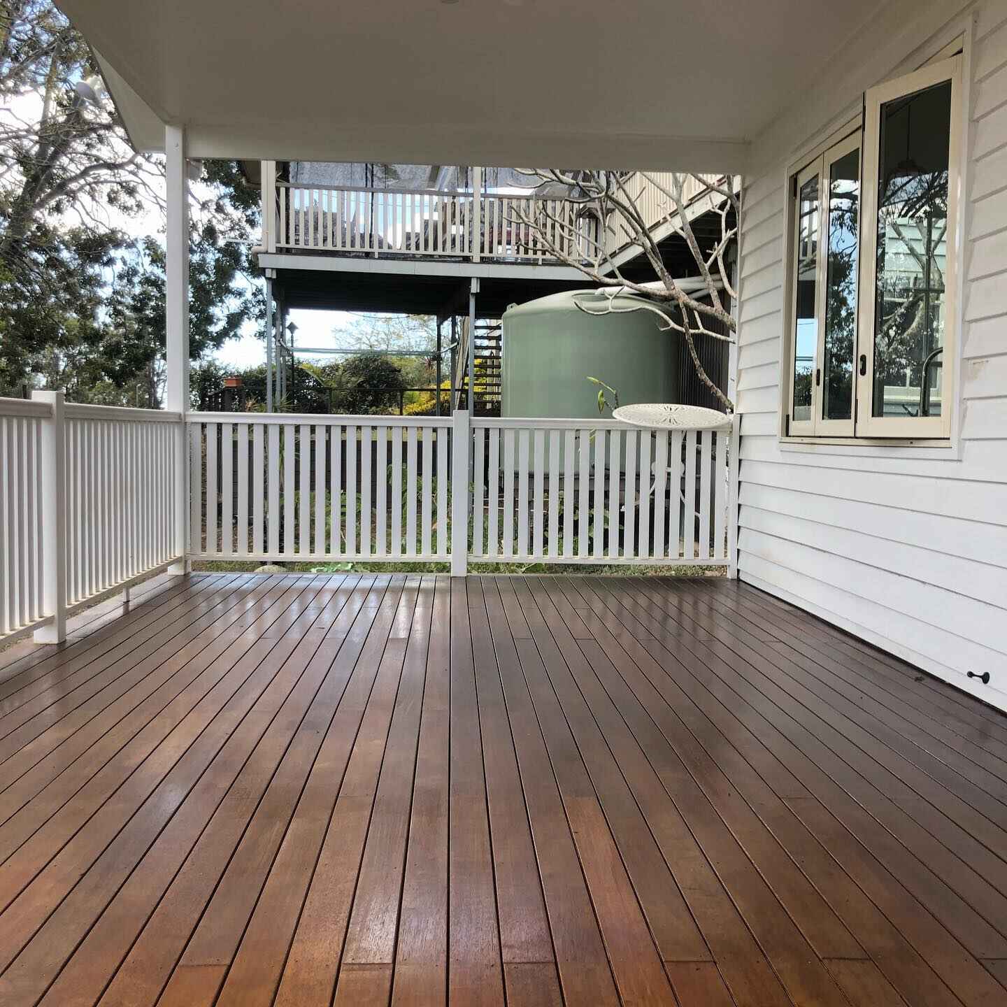 Oiled timber verandah with white balustrade beside a water tank