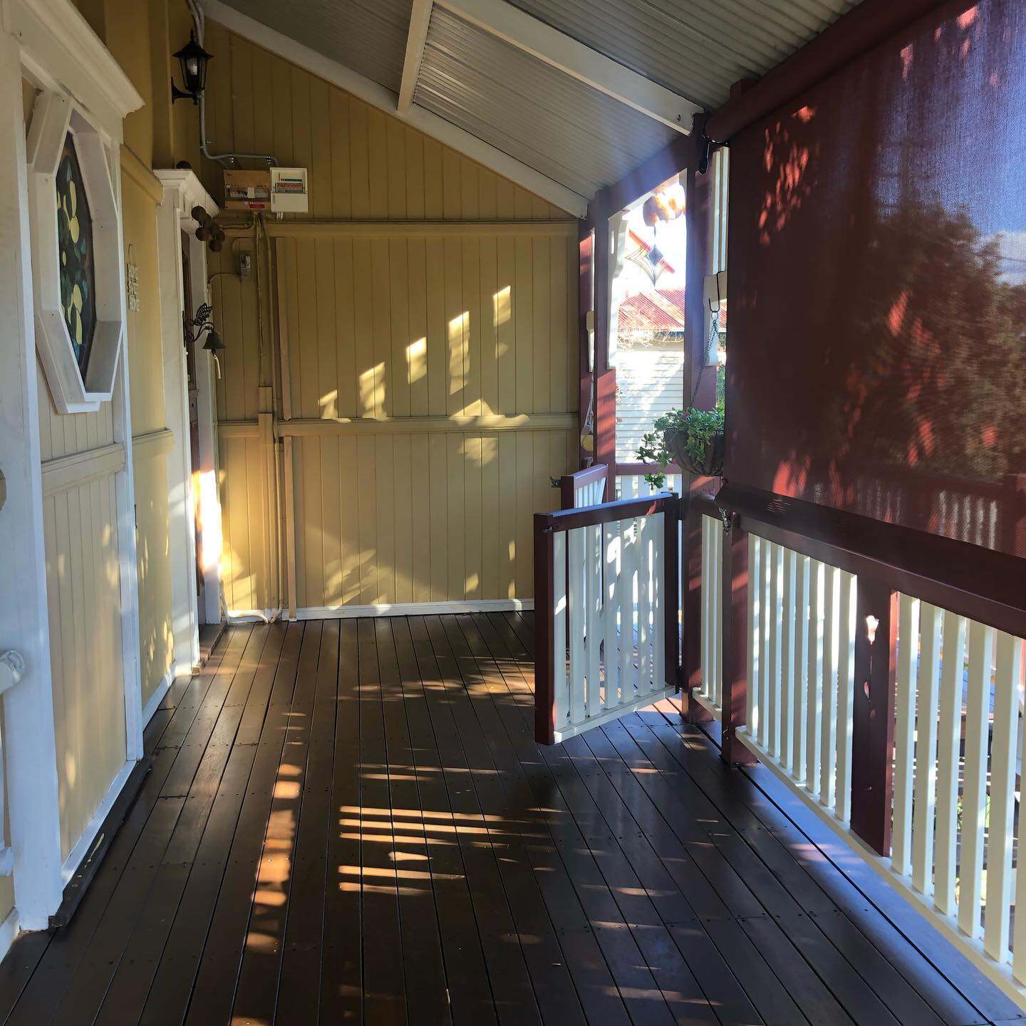 Dark oiled timber verandah with white balustrade and red blind